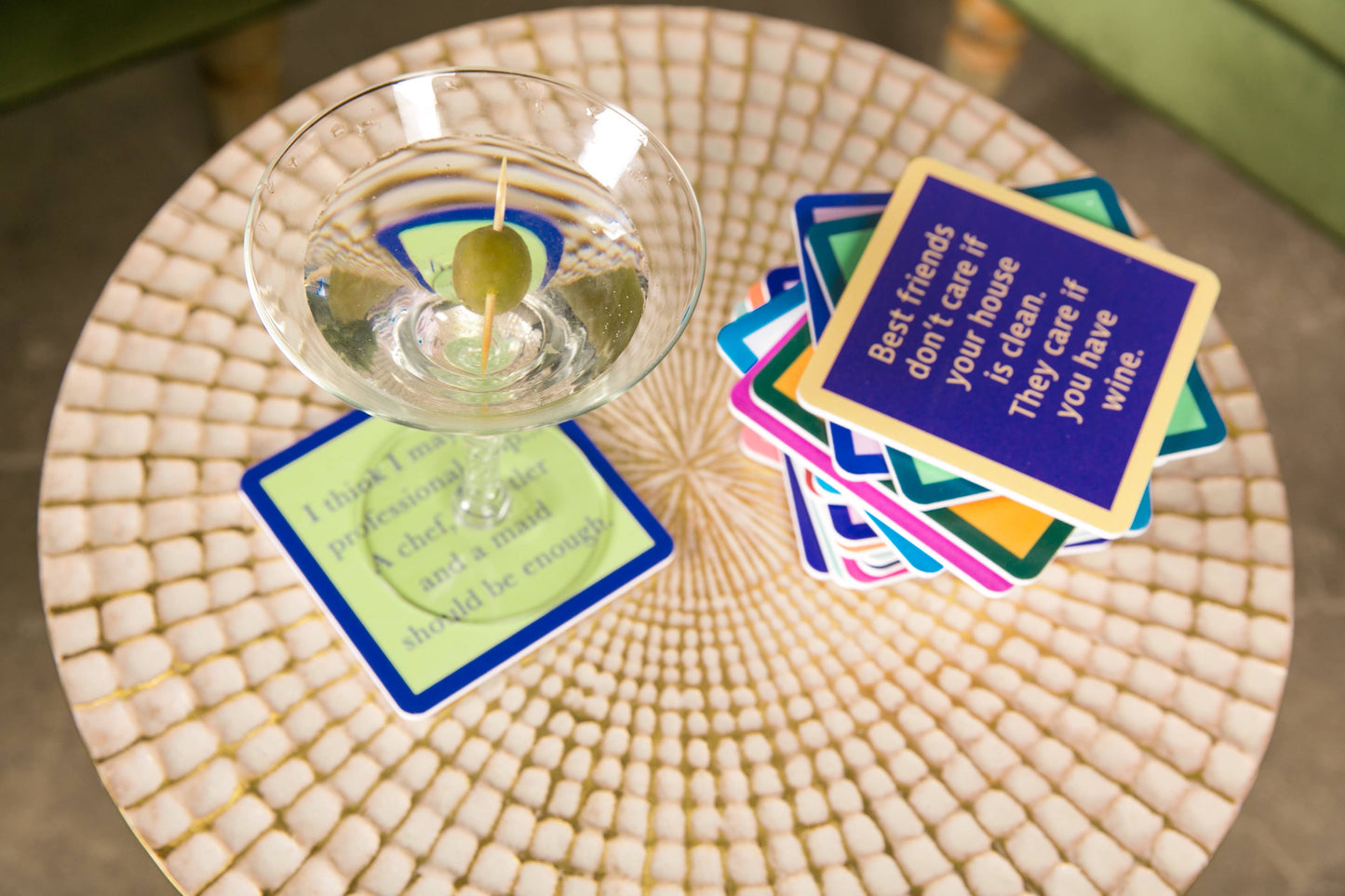Martini with olive on a coaster next to a stack of quote coasters.