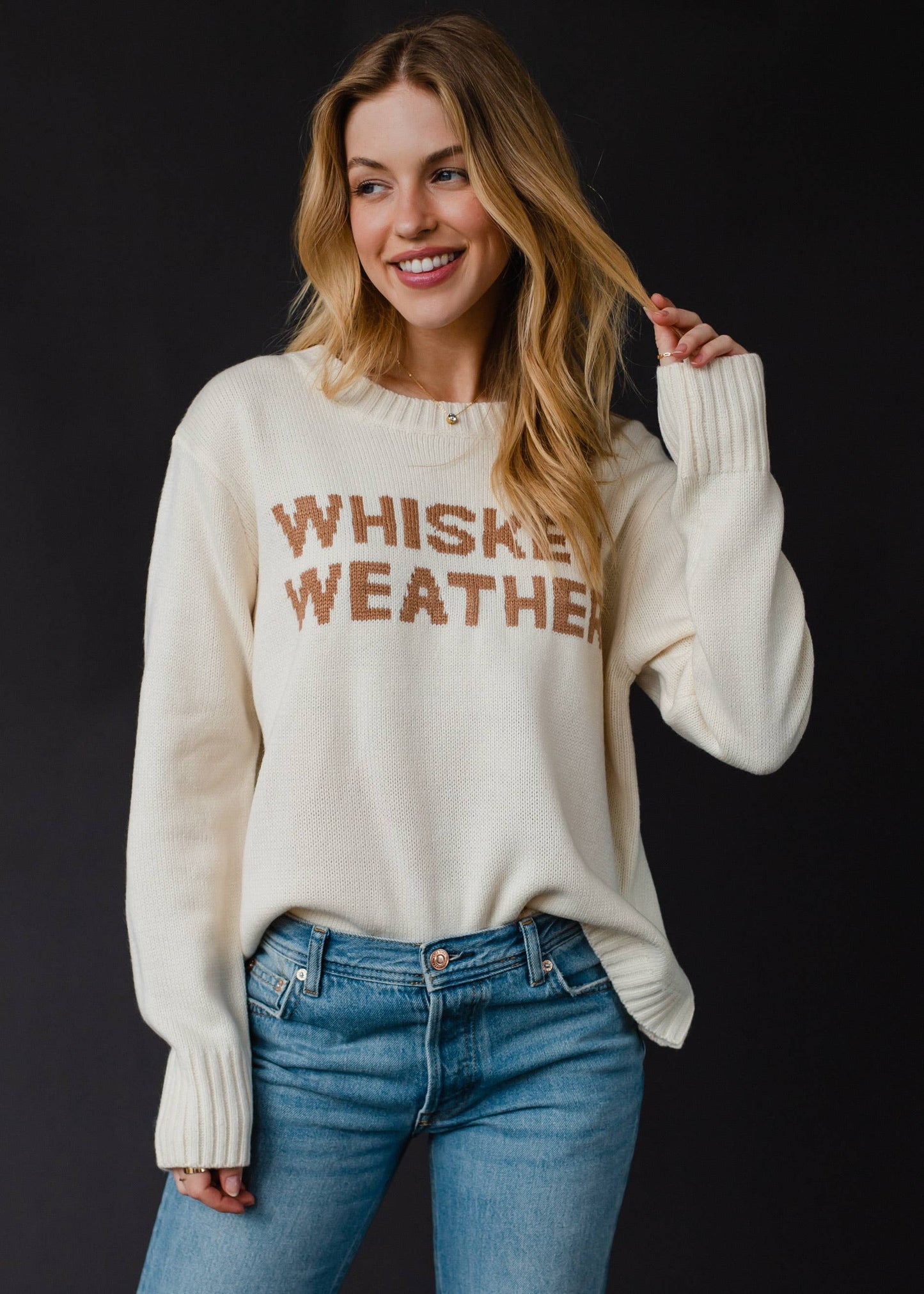 Woman wearing a cream sweater with Whiskey Weather text.