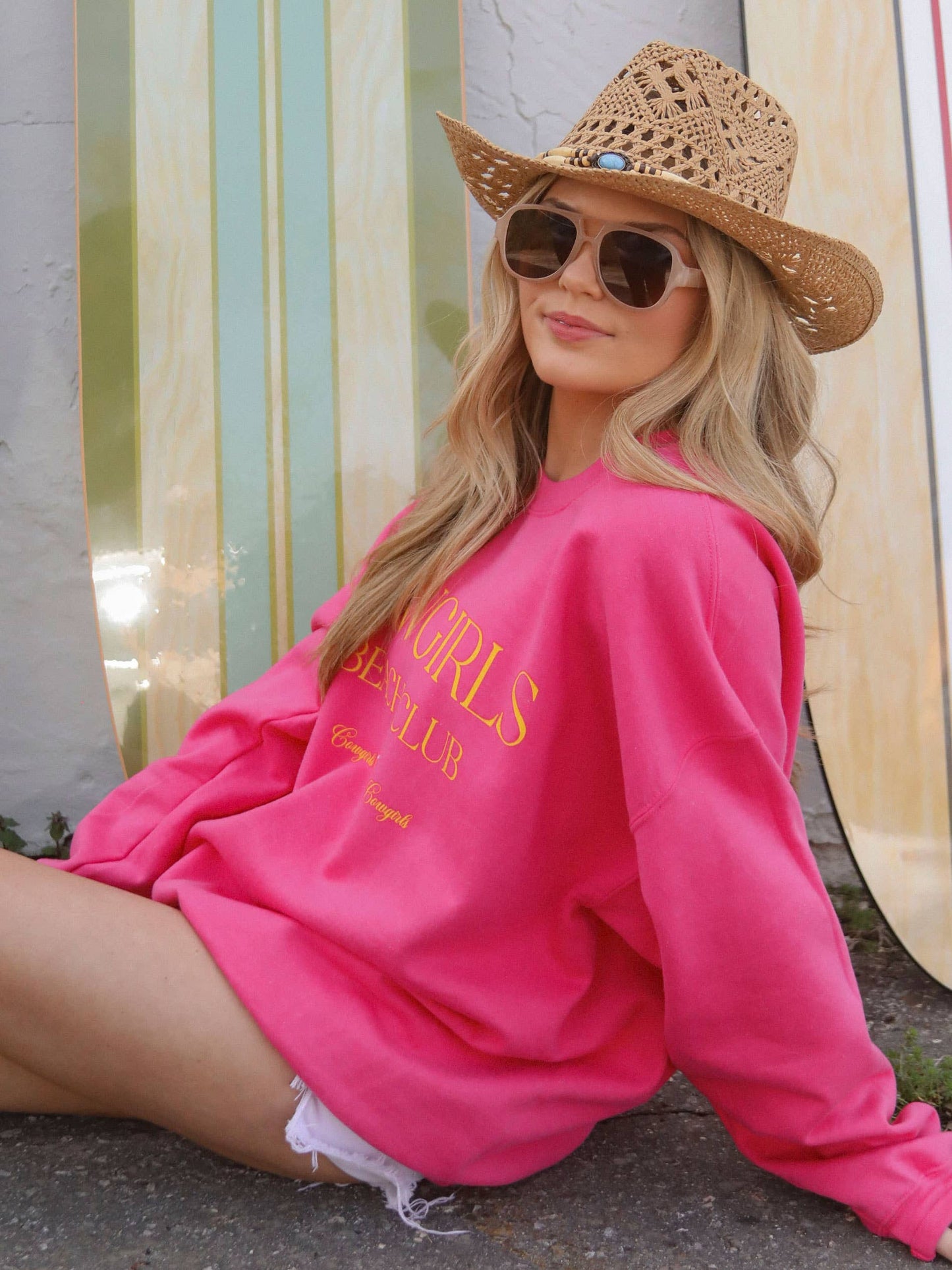 Woman in pink sweatshirt and hat with surfboards.