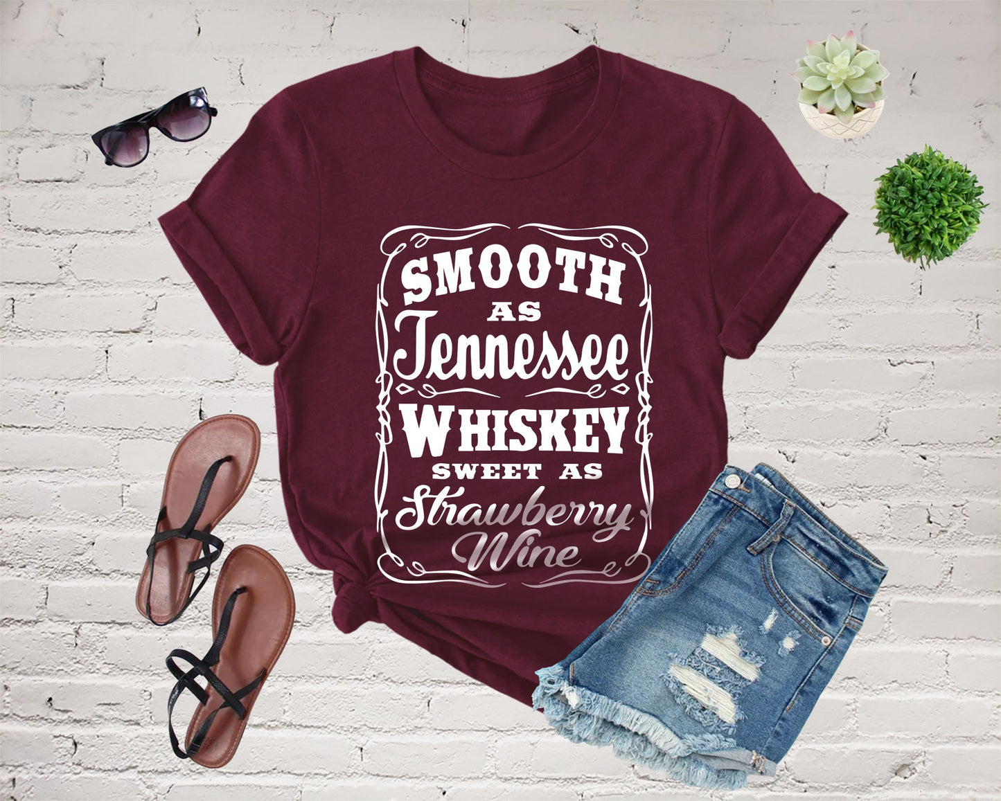 Burgundy t-shirt with text, denim shorts, sandals, and sunglasses.