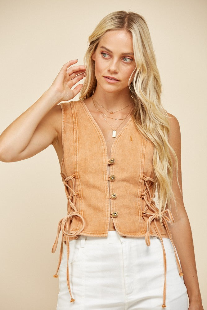 Woman wearing a tan vest and white pants.