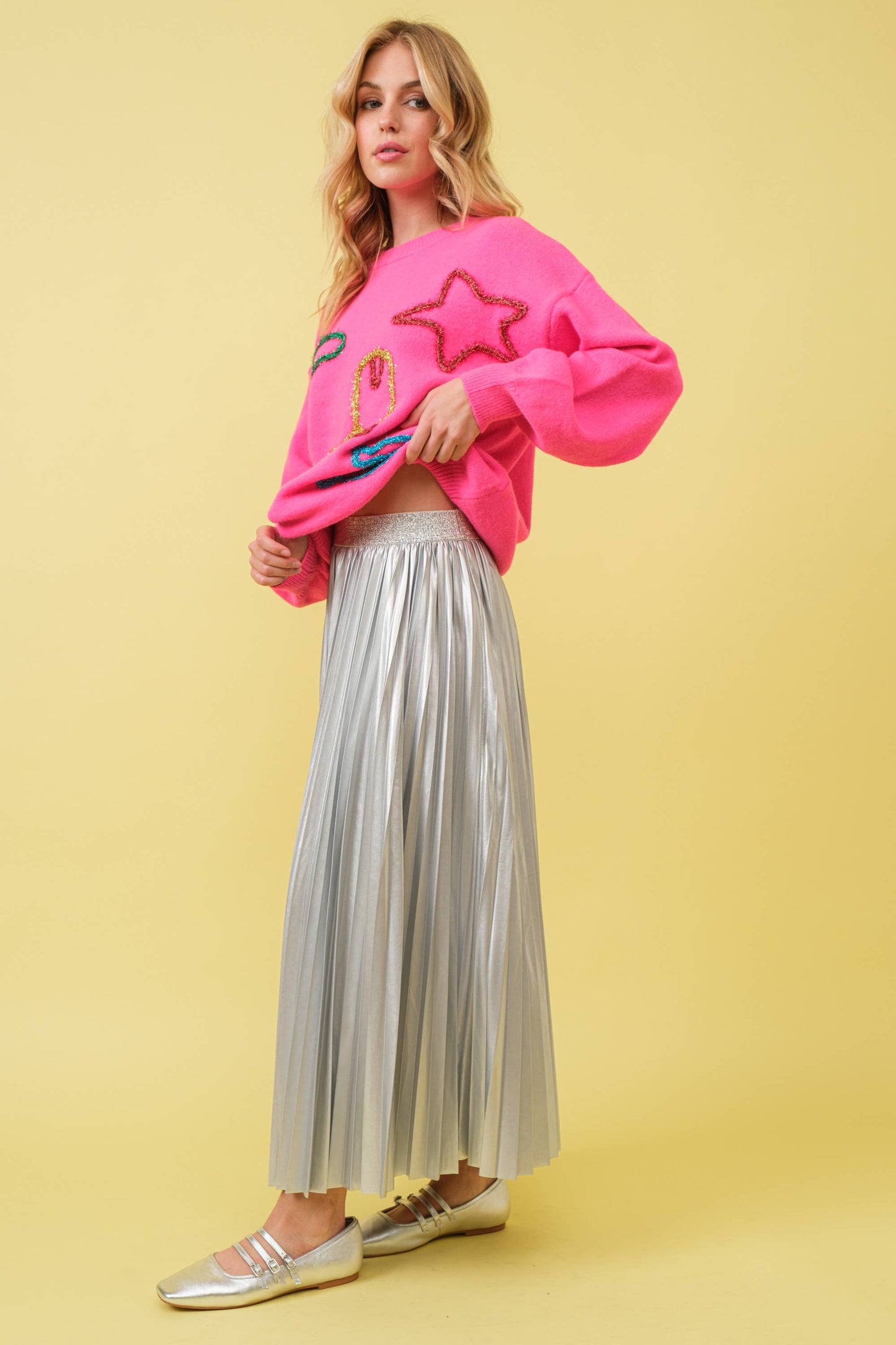 Woman in pink sweater and silver pleated skirt.