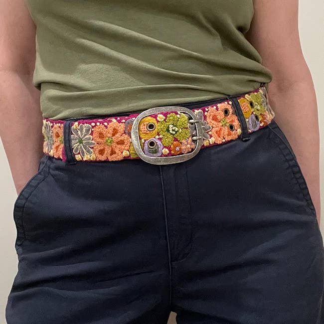Person wearing a floral embroidered belt and dark pants.