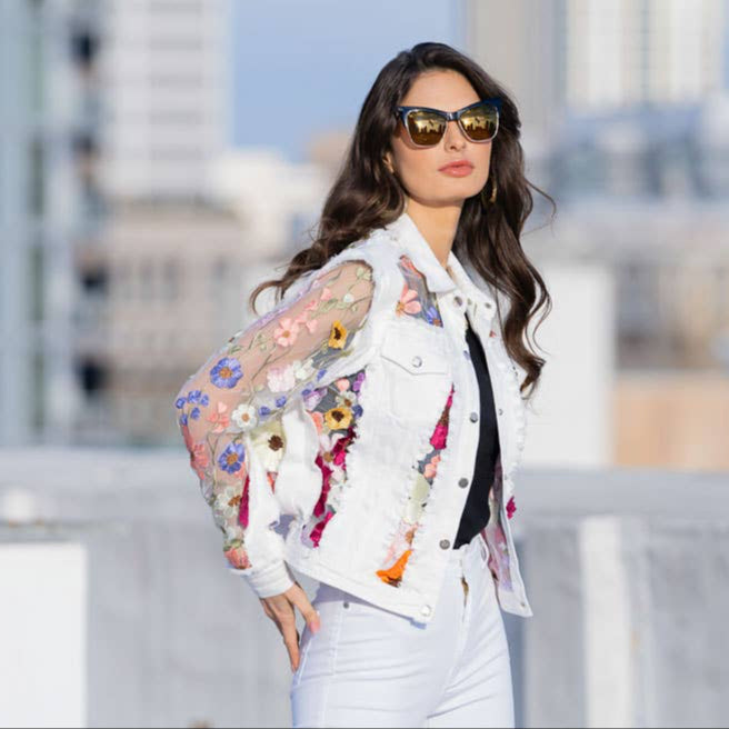 Woman in sunglasses and white floral jacket.