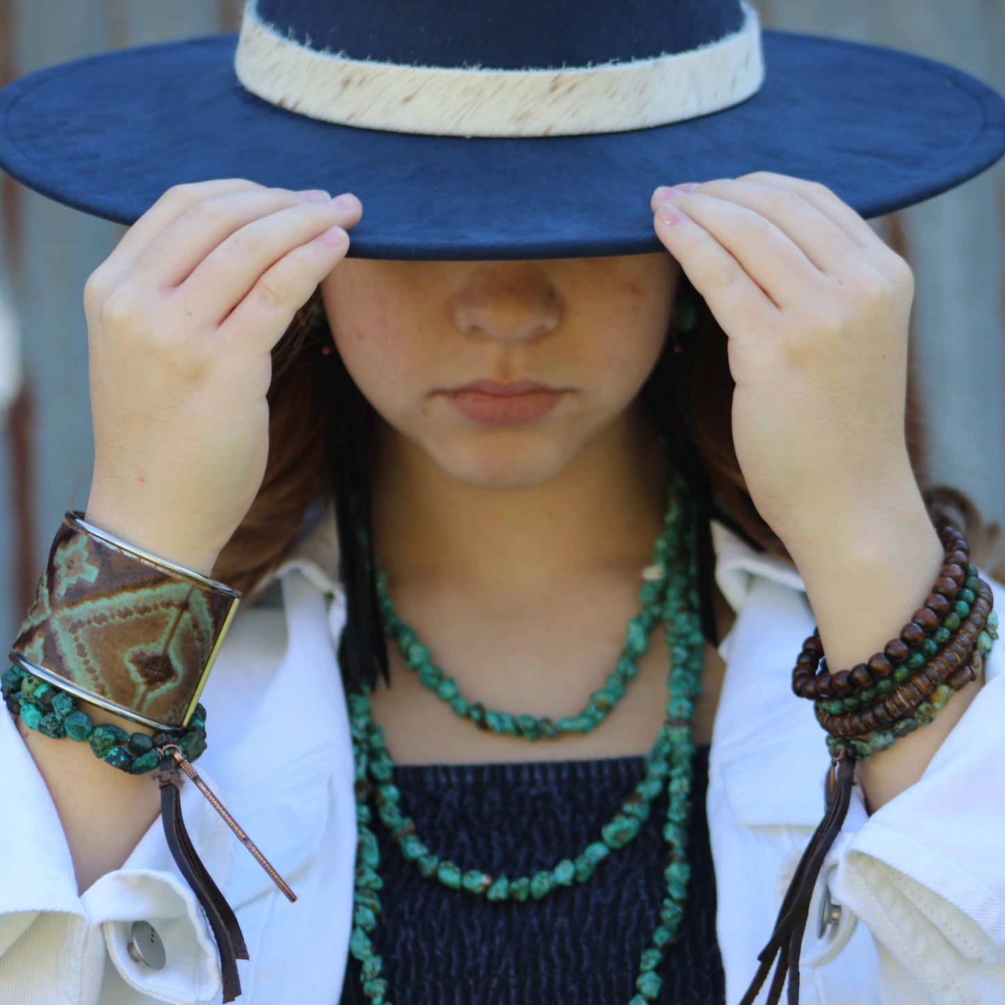 Woman wearing hat and jewelry, covering face.