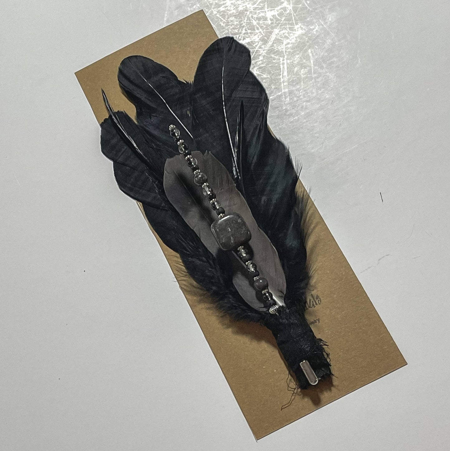 Black feather brooch on cardboard.