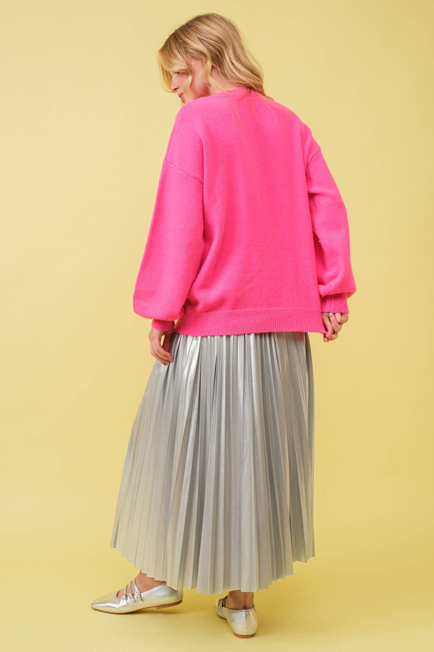 Woman in pink sweater and silver pleated skirt.