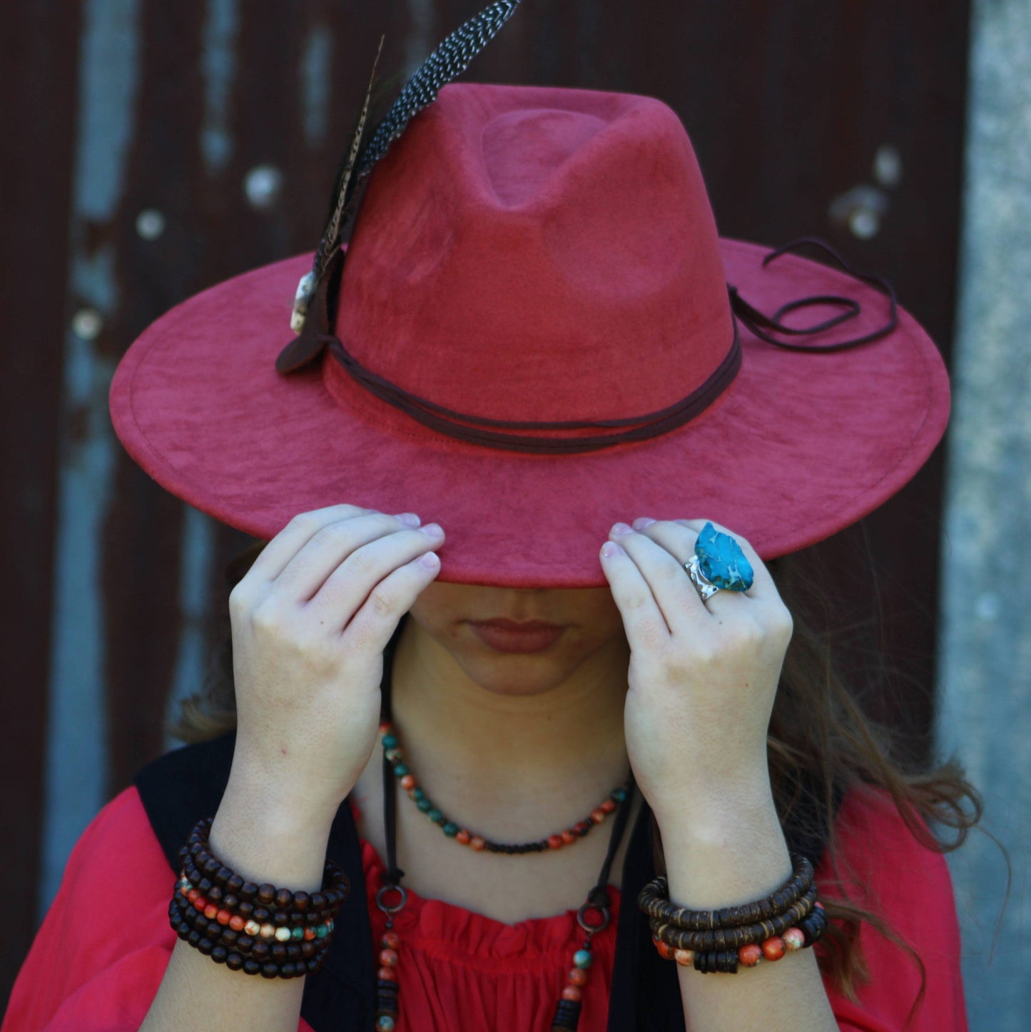 Person wearing red hat and jewelry, covering face.