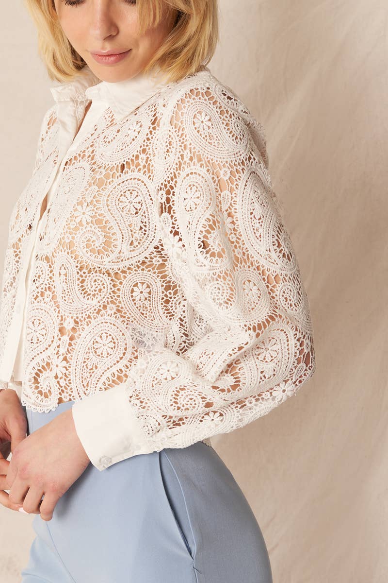 Woman wearing a white lace paisley shirt and blue pants.