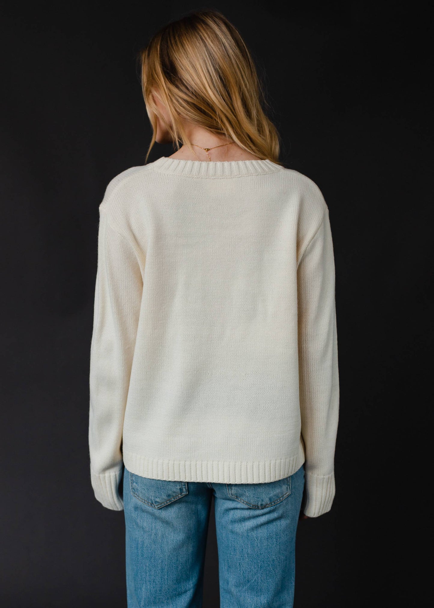 Woman in a cream sweater and jeans, viewed from the back.