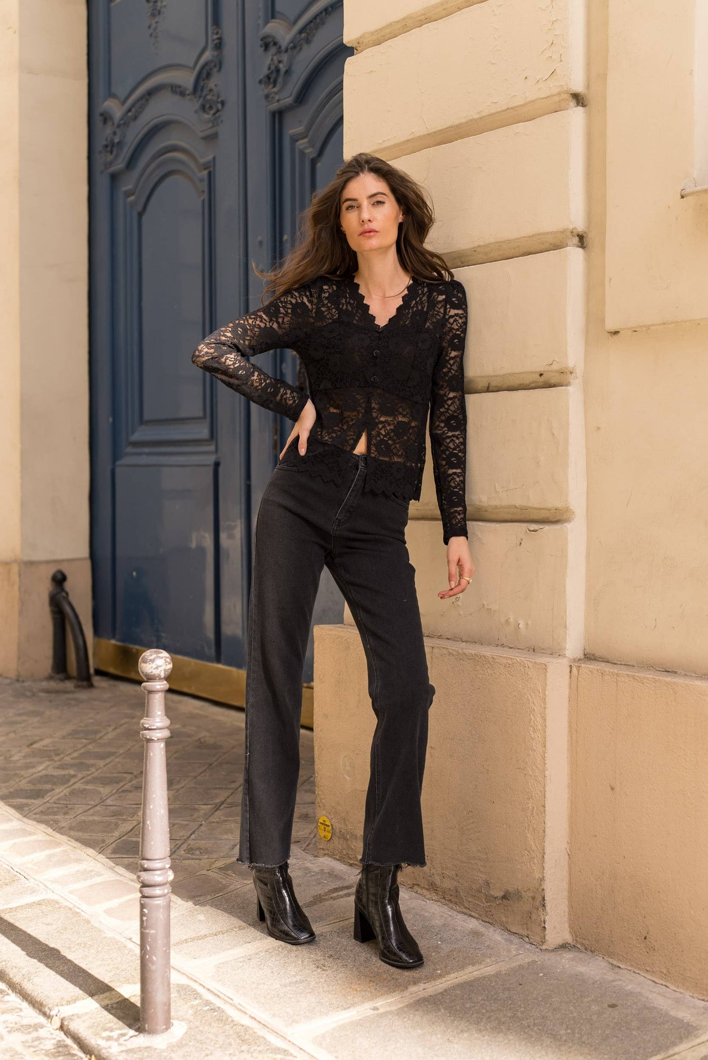 Woman in black lace top and pants posing outdoors.
