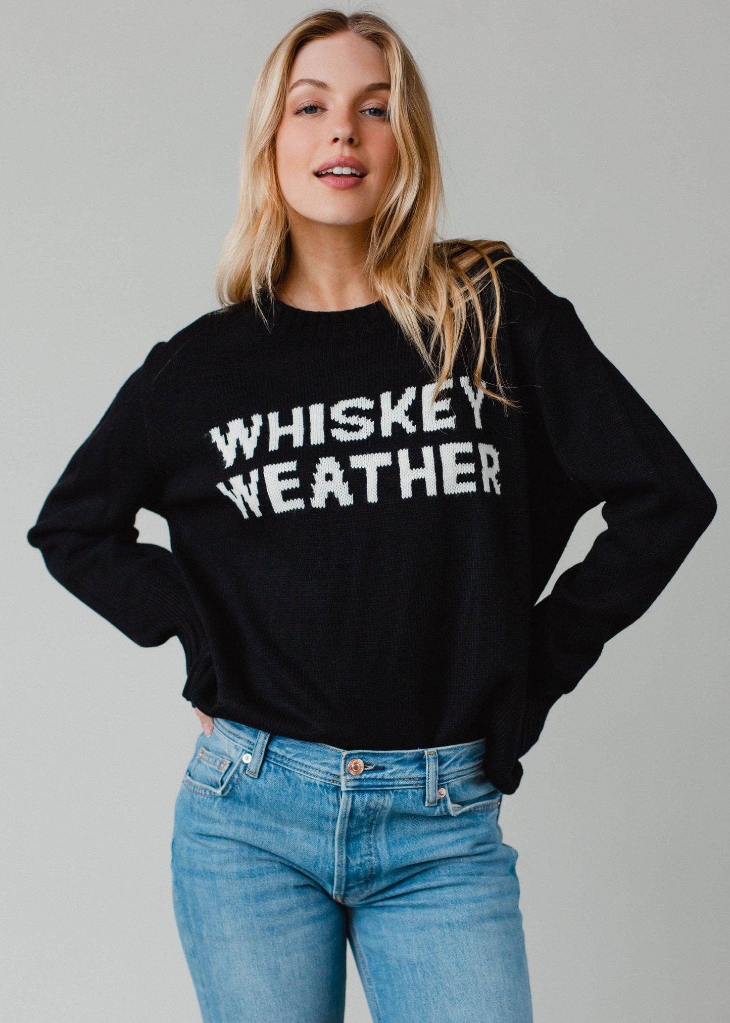 Woman wearing a black sweater with WHISKEY WEATHER on it.