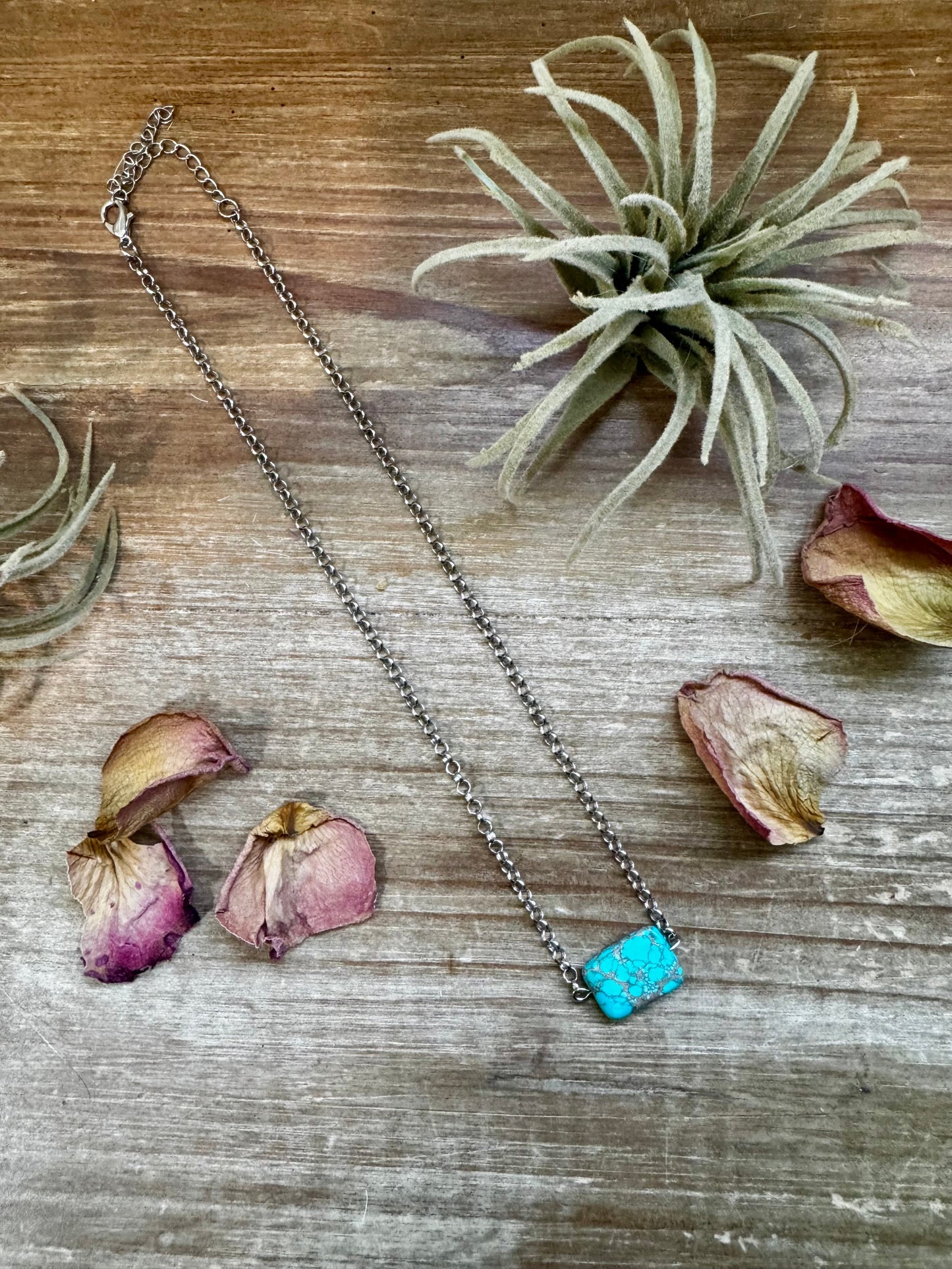 Turquoise stone necklace (BC239849) on rustic wood with flowers.