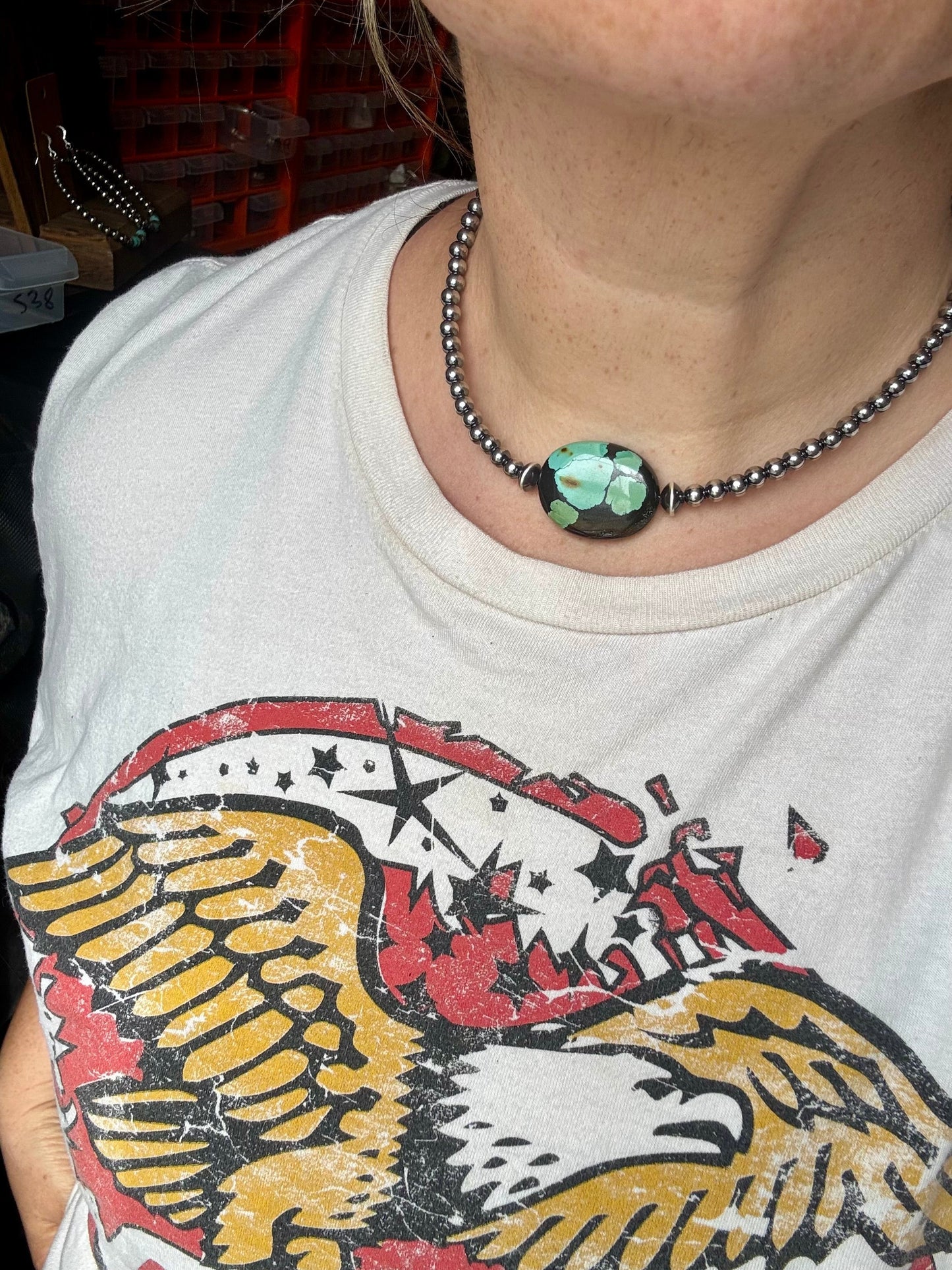 Turquoise necklace on a person wearing a graphic tee.