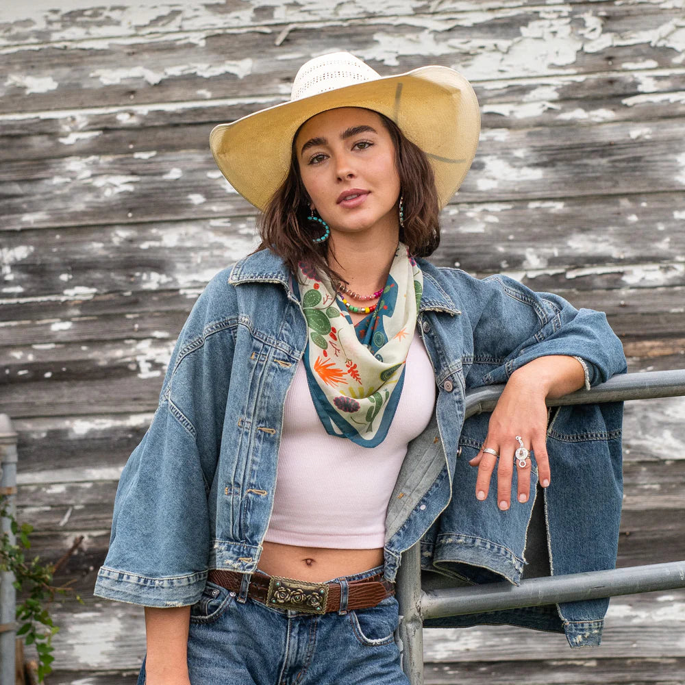 Cowgirl in denim jacket and hat leaning on fence