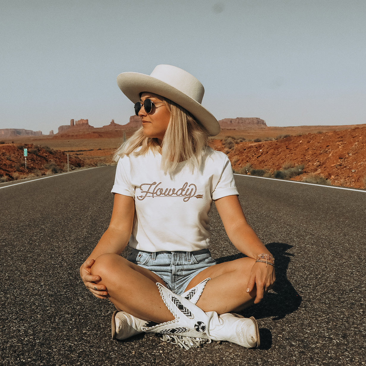 Woman in Howdy tee sitting on road