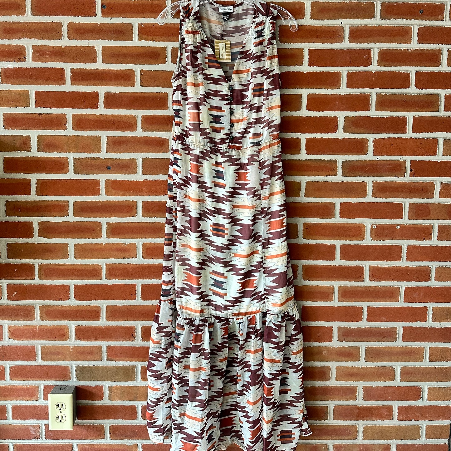 Sleeveless patterned maxi dress hanging on brick wall.