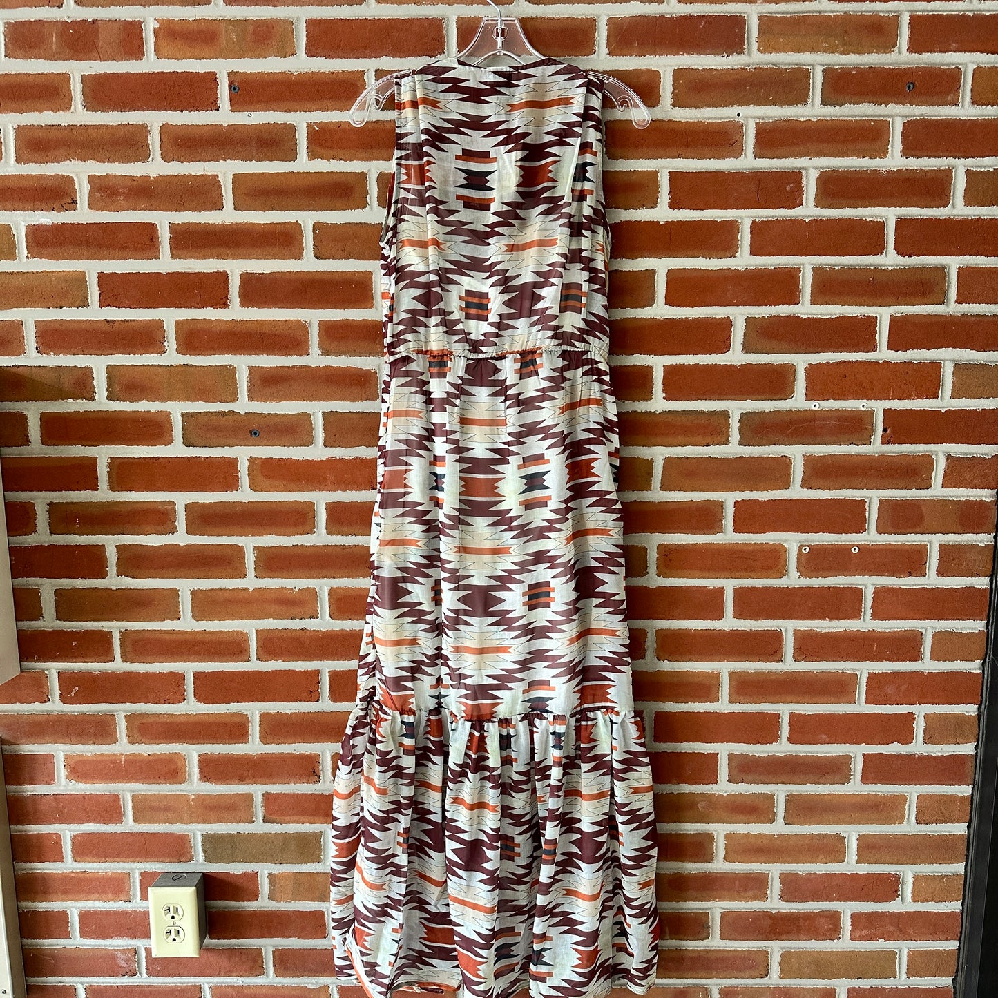 Sleeveless patterned dress hanging on a brick wall.