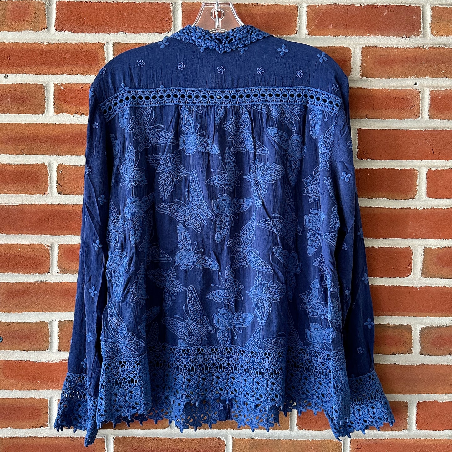 Blue embroidered shirt hanging on a brick wall.