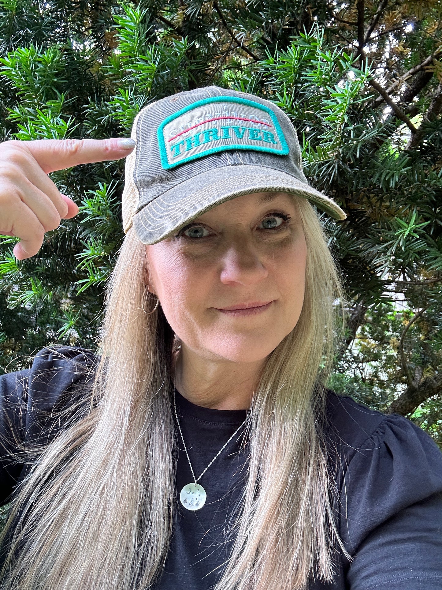 Woman wearing a THRIVER hat and pointing.