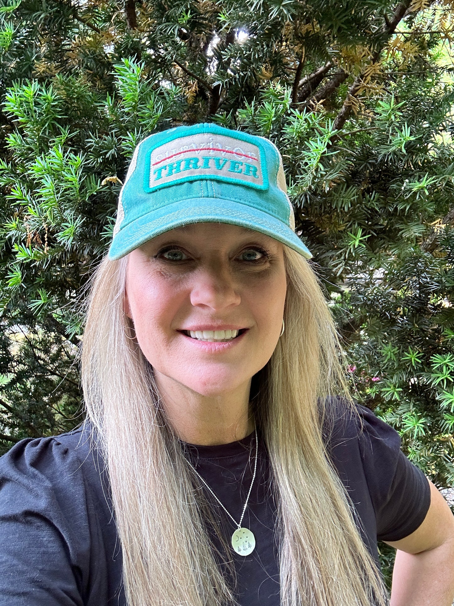 Woman wearing a turquoise hat with THRIVER on it.