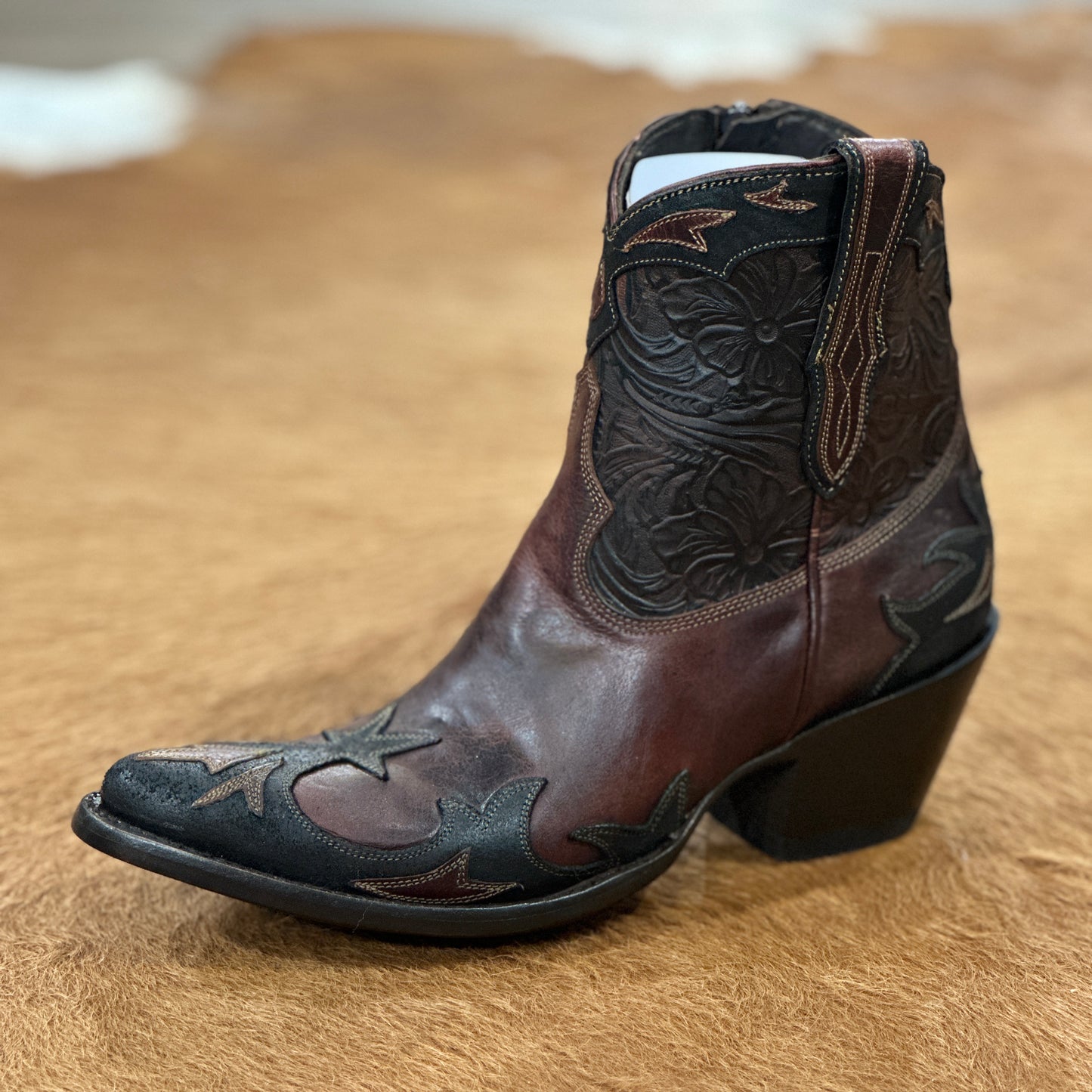 Brown and black leather cowboy boot on brown surface.