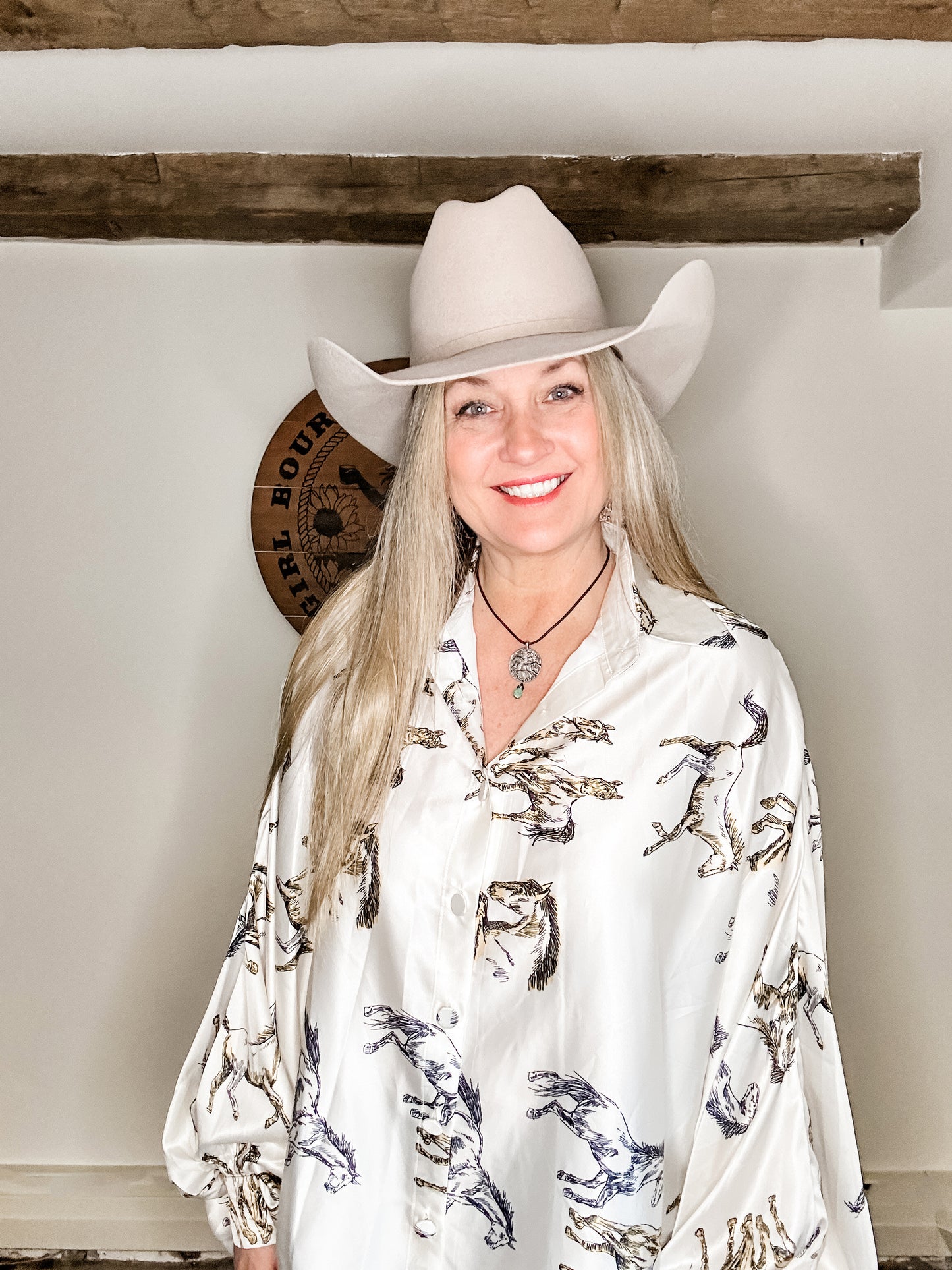 Woman in cowboy hat and horse-print shirt smiles at the camera.