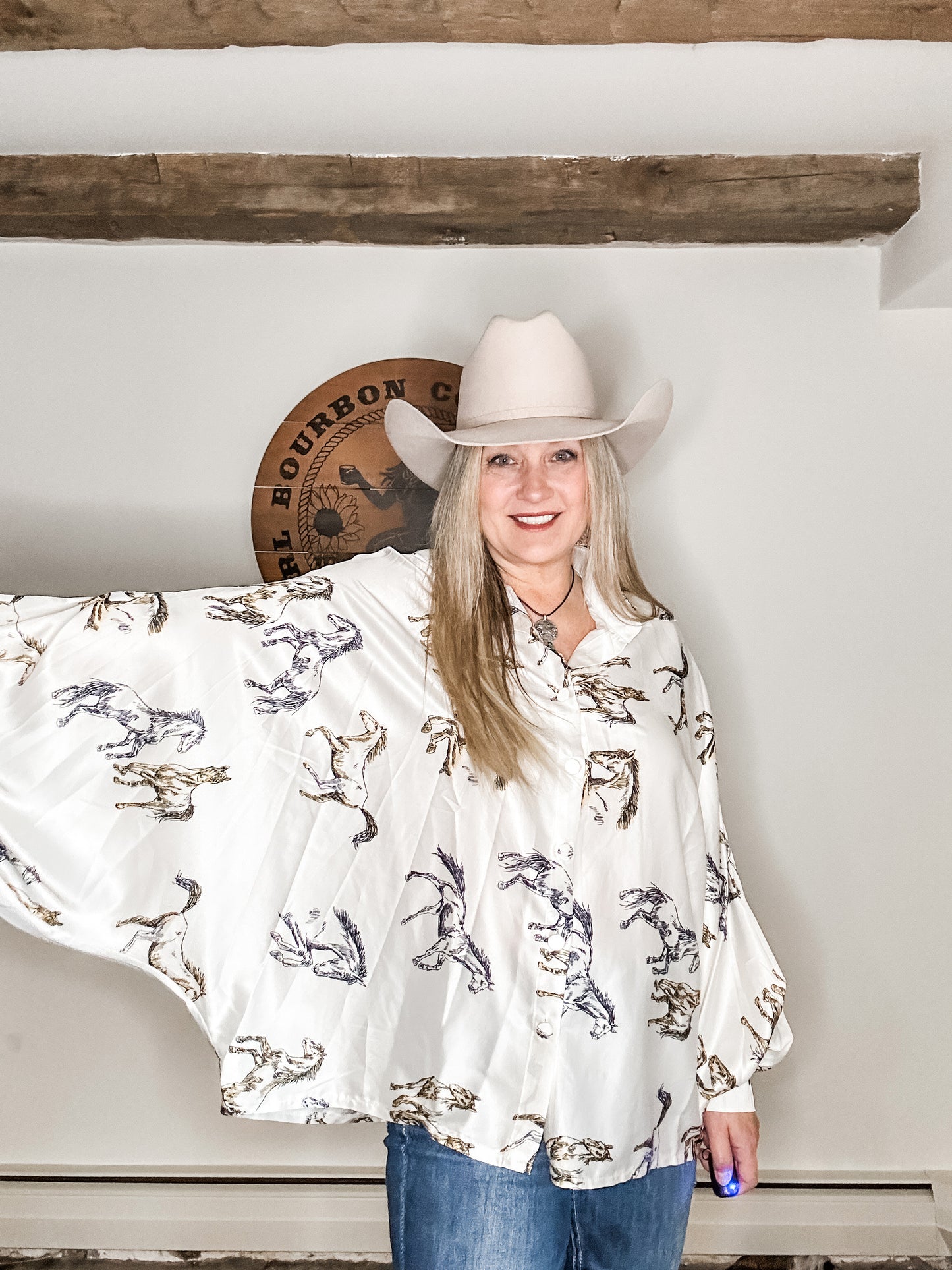 Woman in cowboy hat and horse-print shirt smiling.