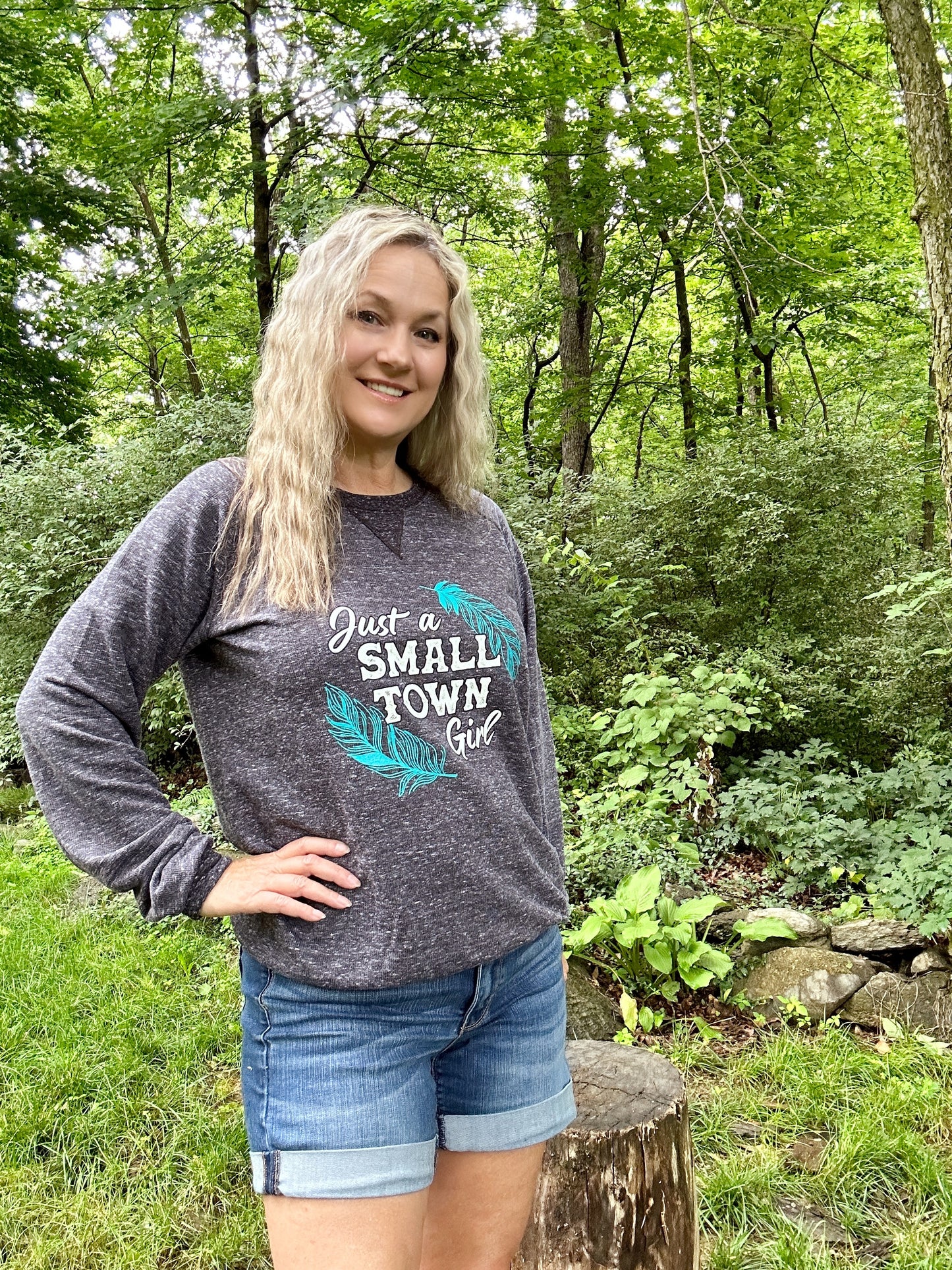 Woman in sweatshirt and shorts smiling in a forest.