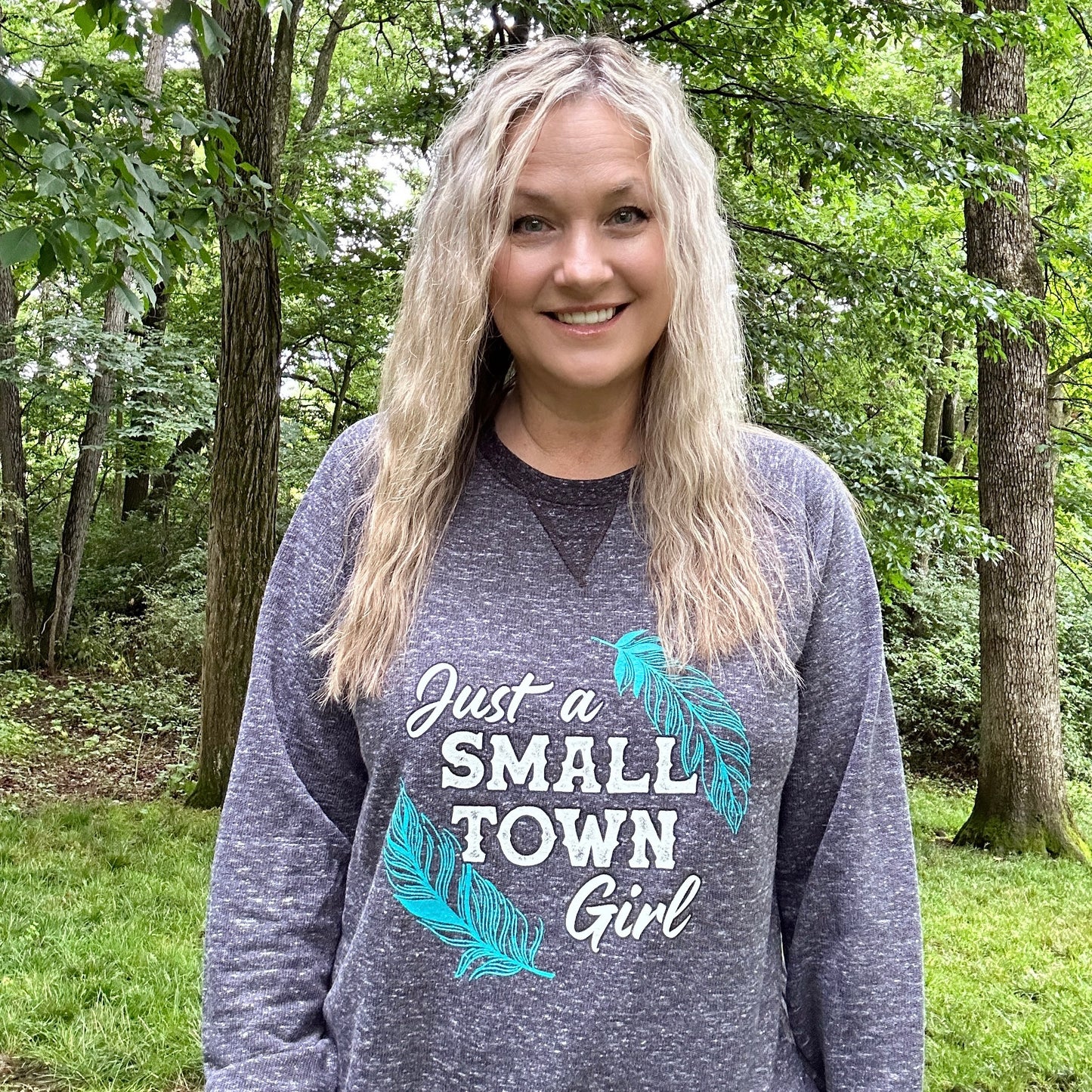Woman with long blonde hair wearing a Just a Small Town Girl sweatshirt.