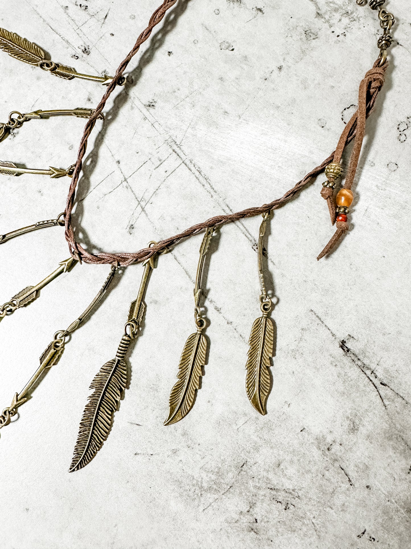 Feather and arrow charm necklace on textured surface.
