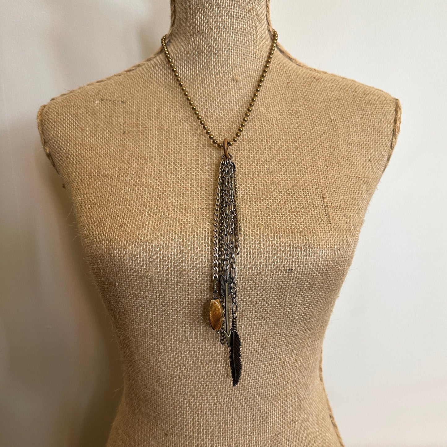 Necklace with chains, stone, and feather on a mannequin.