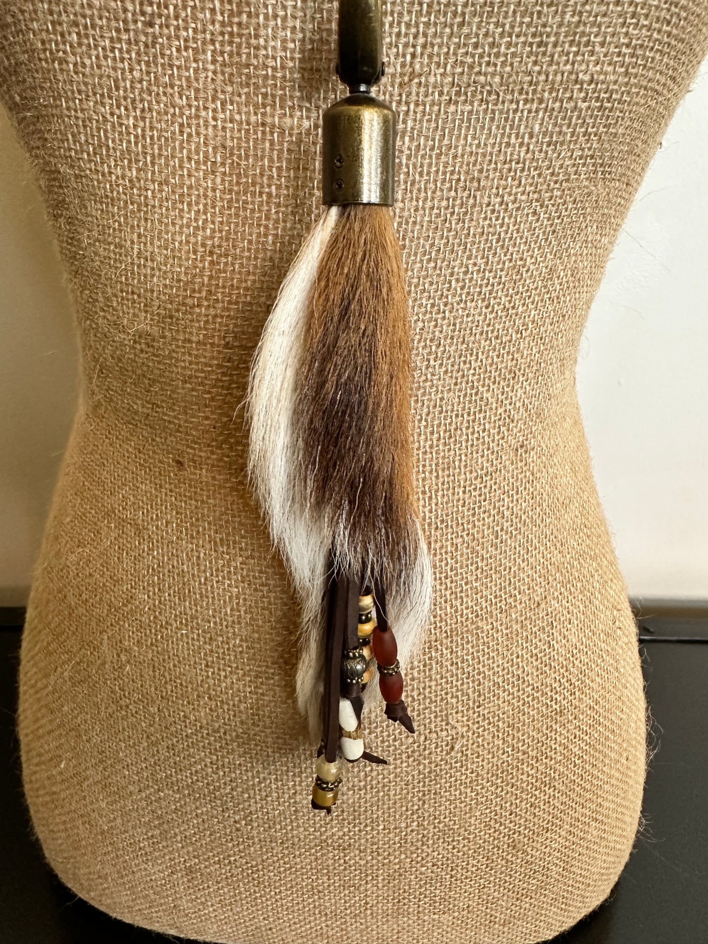 Tassel with fur, beads, and metal cap hanging on a mannequin.