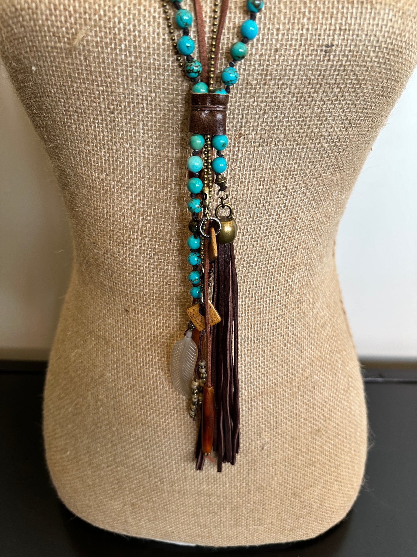 Turquoise beaded necklace with leather tassel on a mannequin.