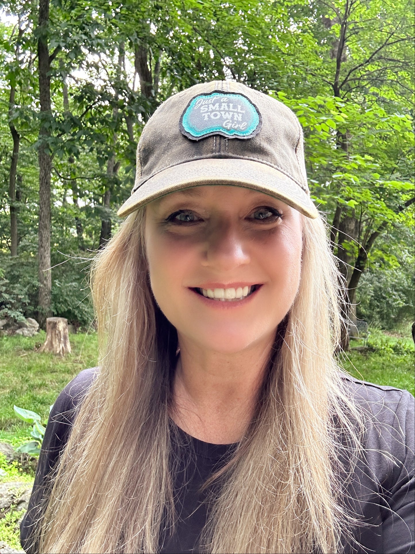 Woman smiling, wearing a hat, in front of trees.