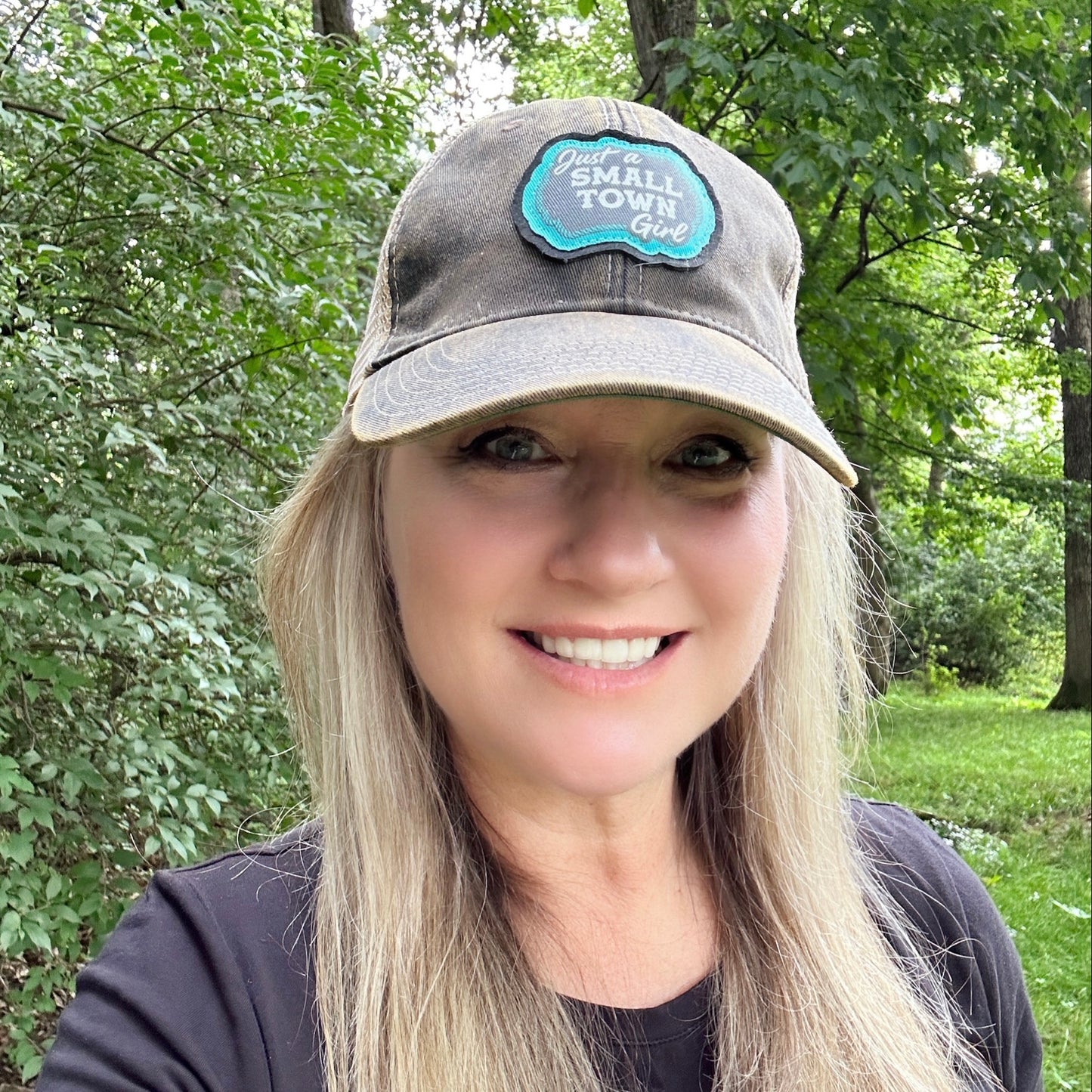 Woman wearing a cap with a teal patch, smiling.