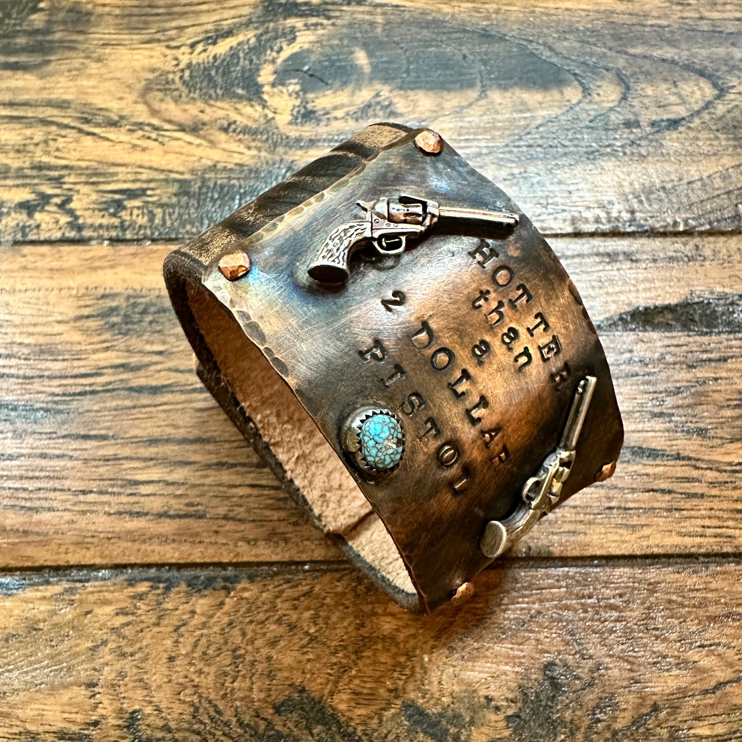 Leather cuff bracelet with guns and text.