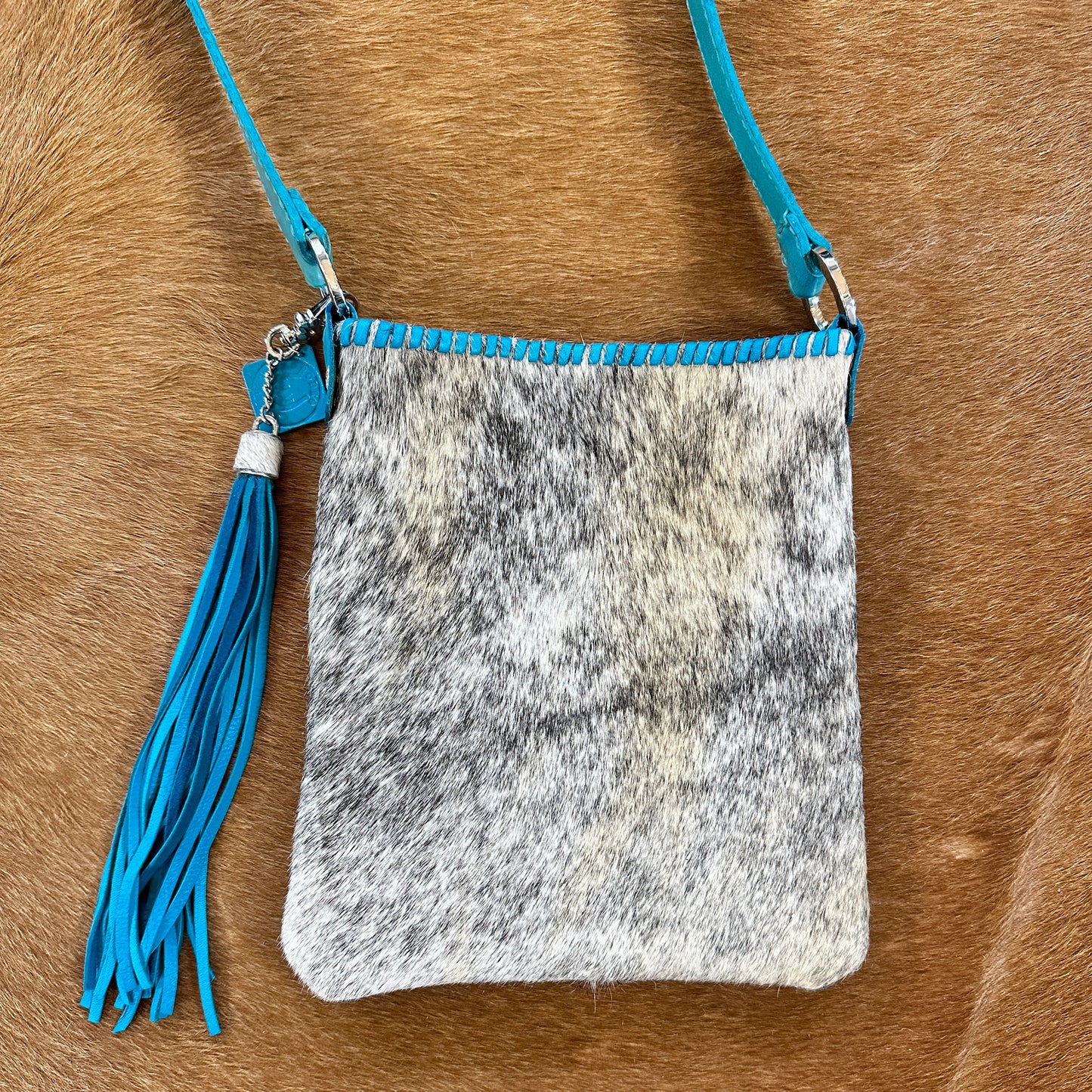 Cowhide crossbody bag with blue accents and tassel.