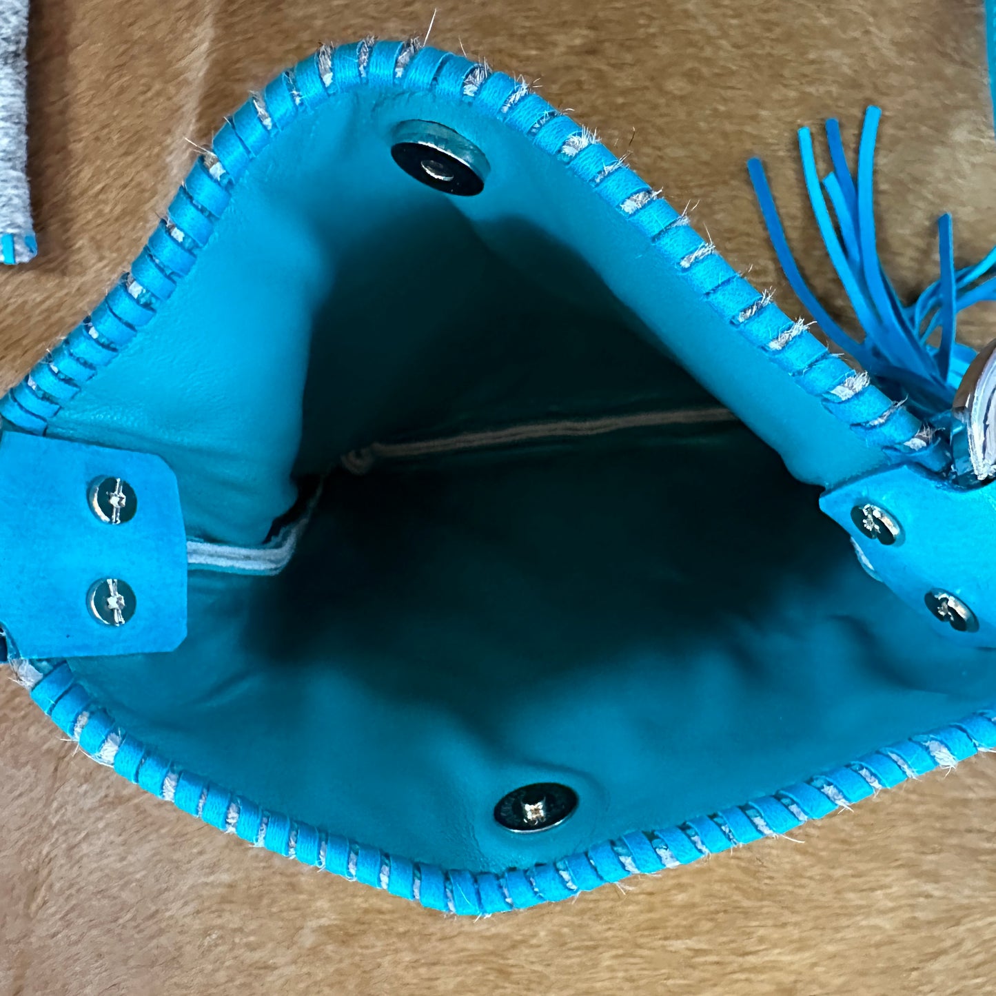 Open turquoise leather bag with tassels.