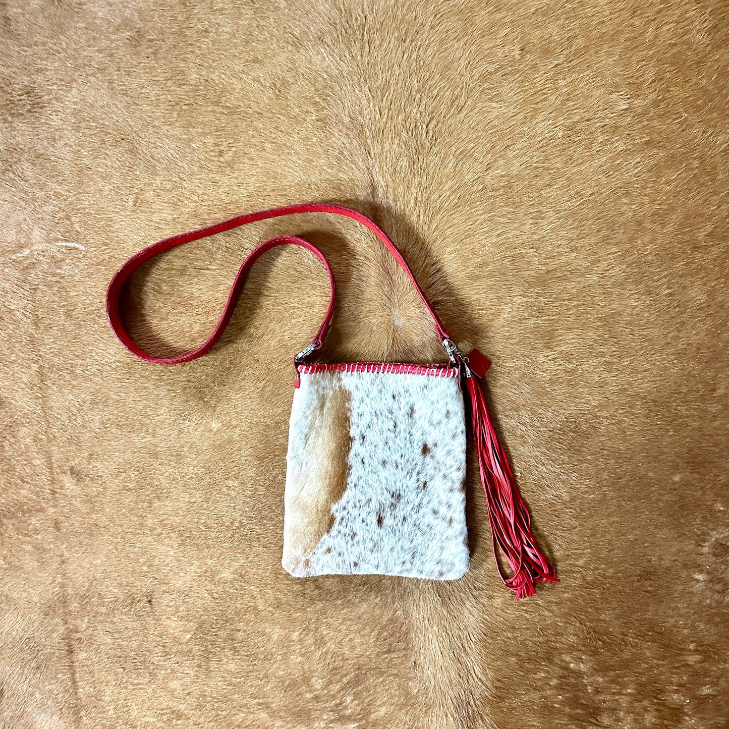 Small, white and tan cowhide purse with red strap and tassel.