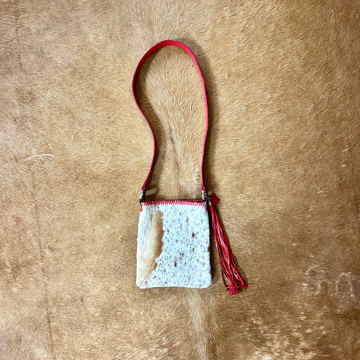 Small, white and tan purse with red strap and tassel.