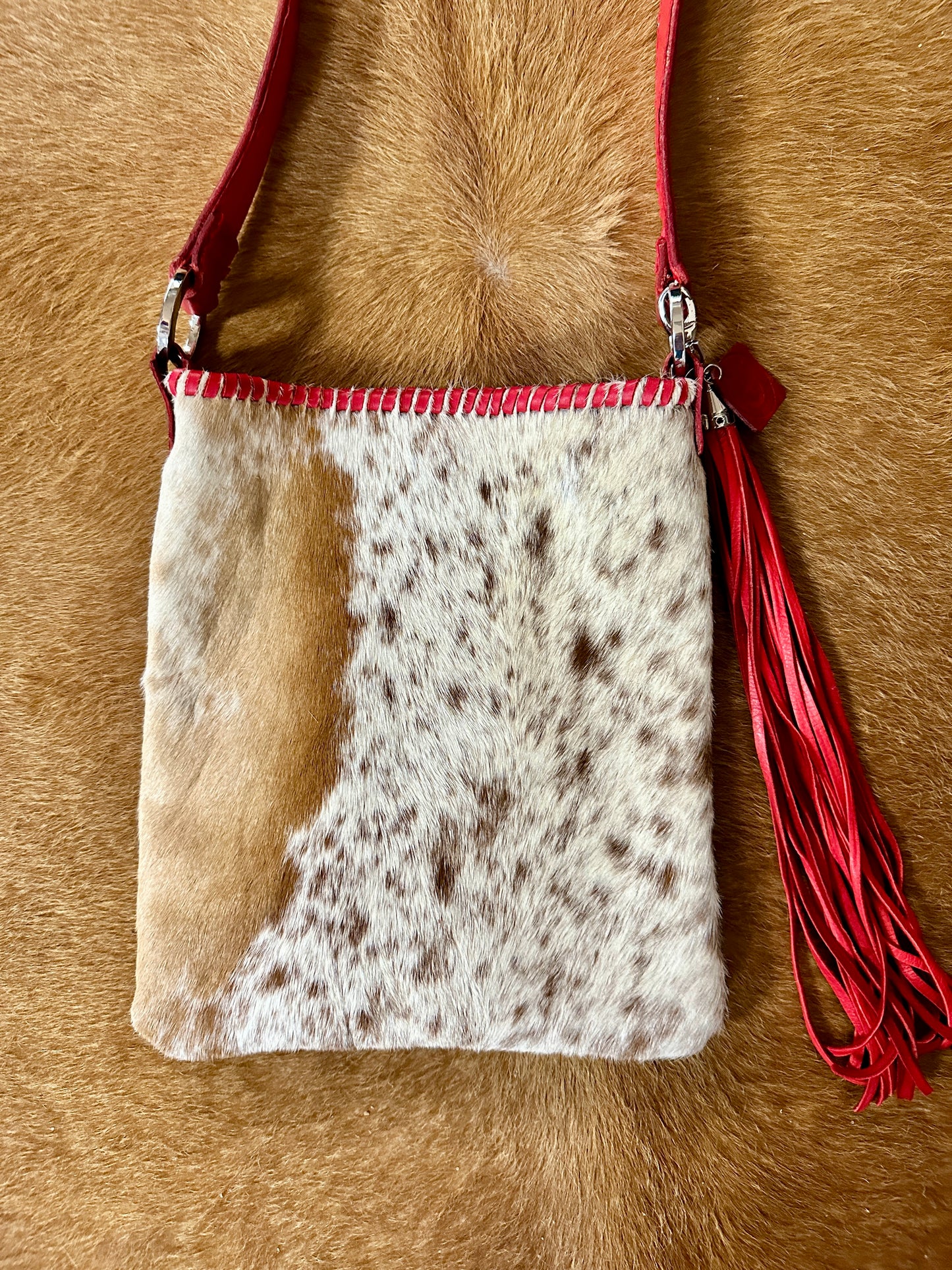 Cowhide crossbody bag with red strap and tassel.