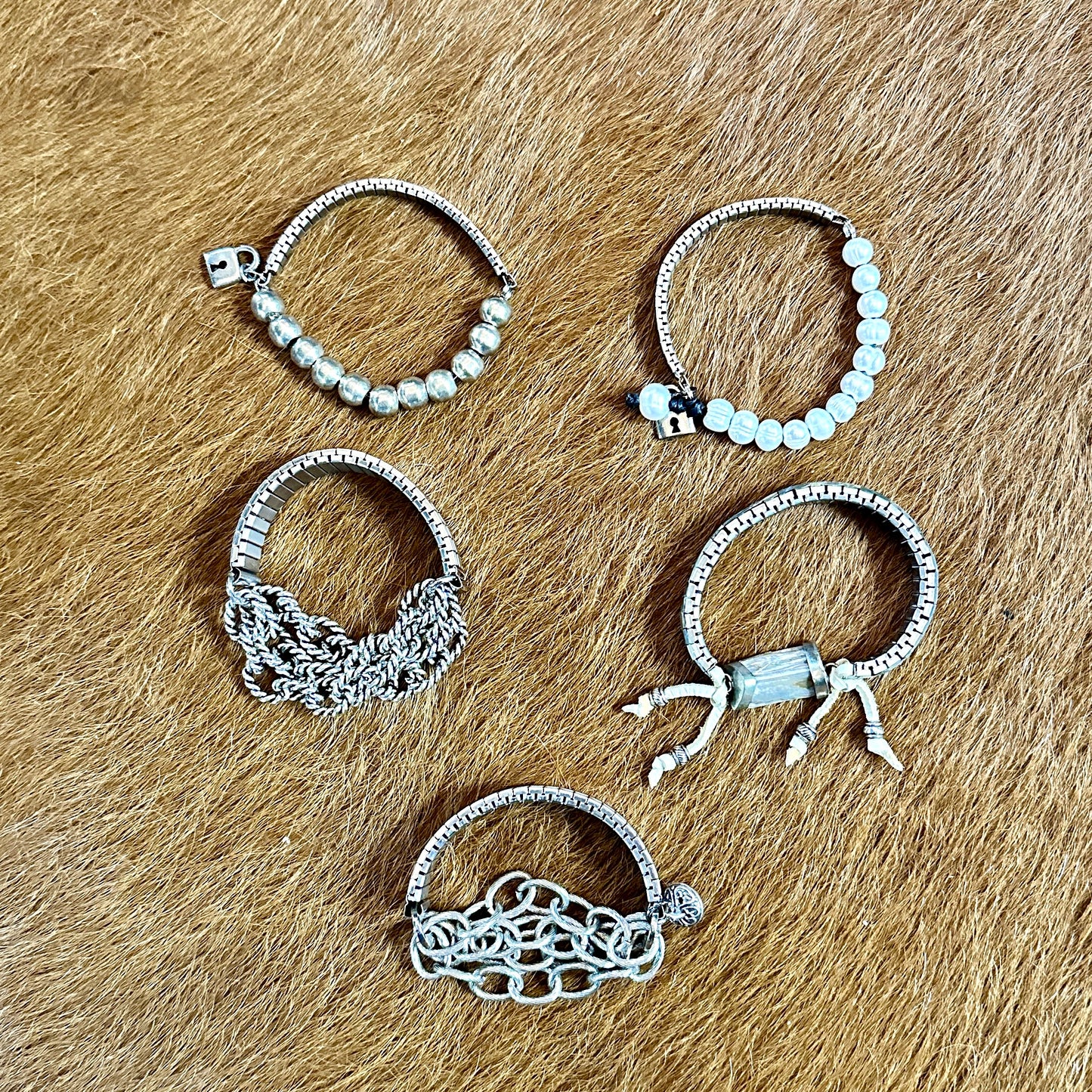 Five silver bracelets on a brown surface.