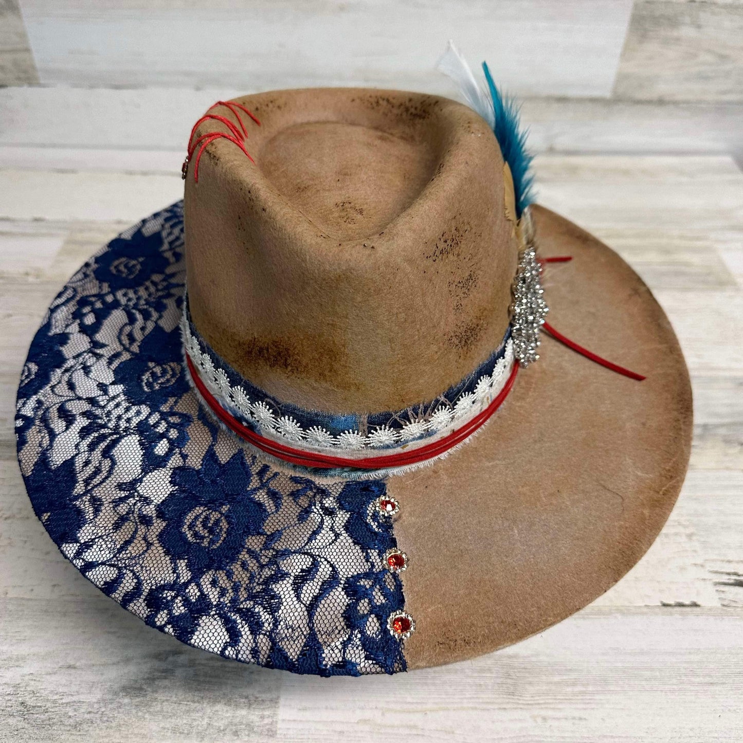 Brown cowboy hat with blue lace brim and feathers.