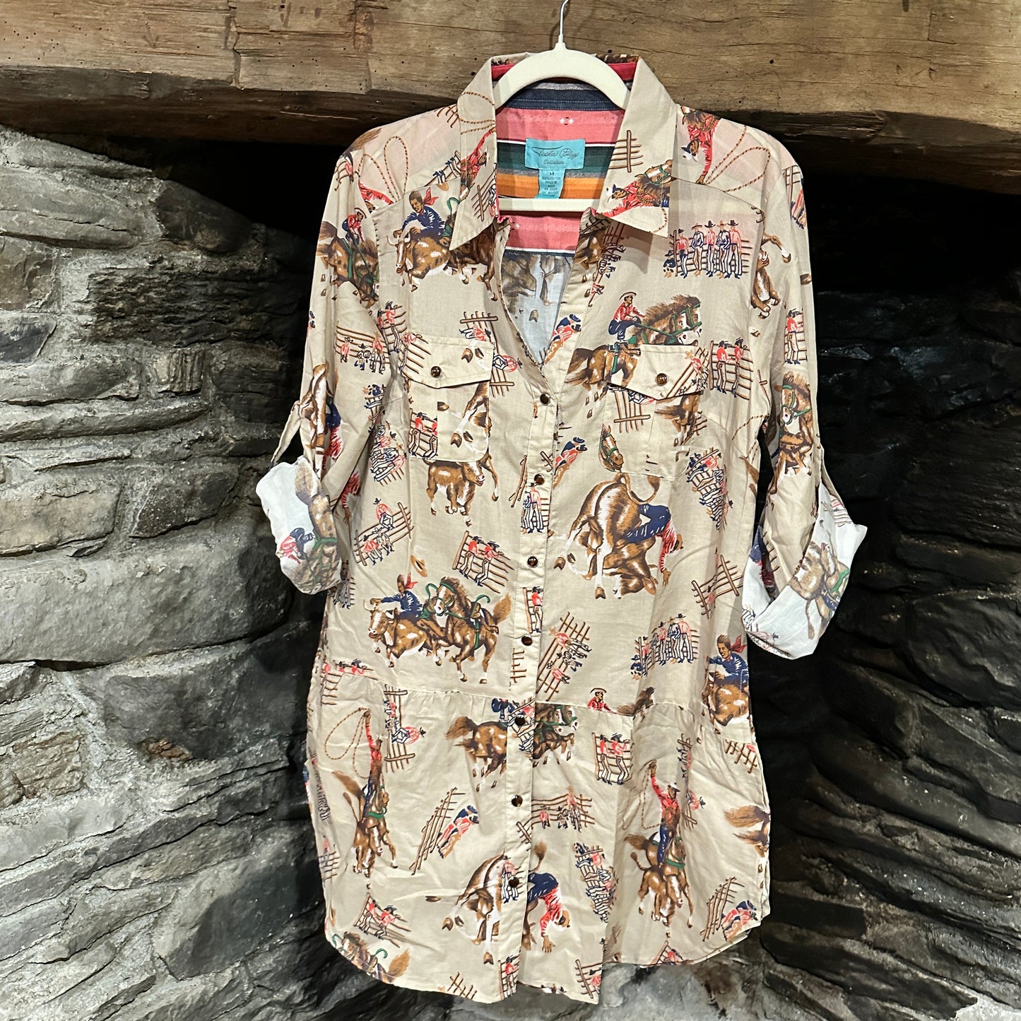 Cowboy print button-down shirt hanging on a wooden surface.