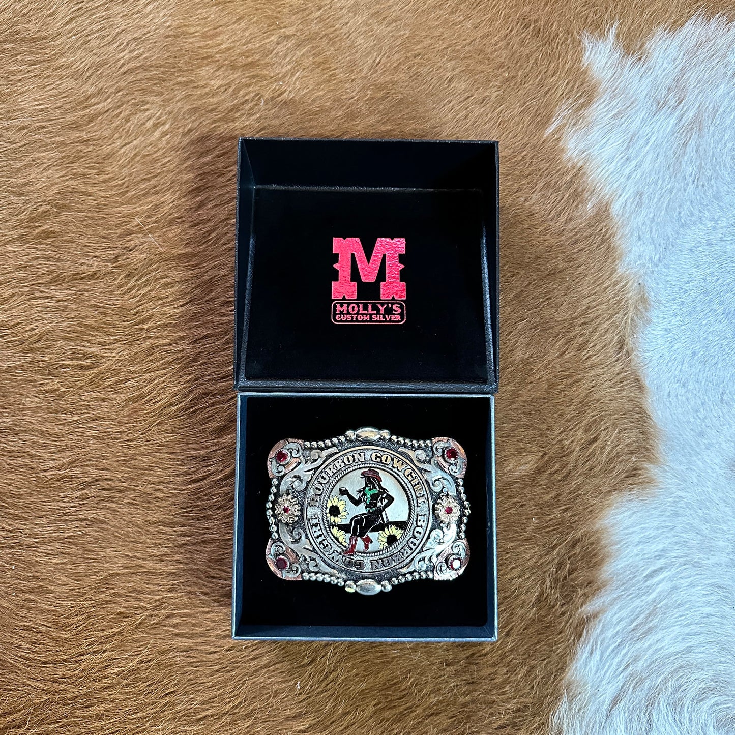 Open box with a decorative belt buckle on a brown and white background.