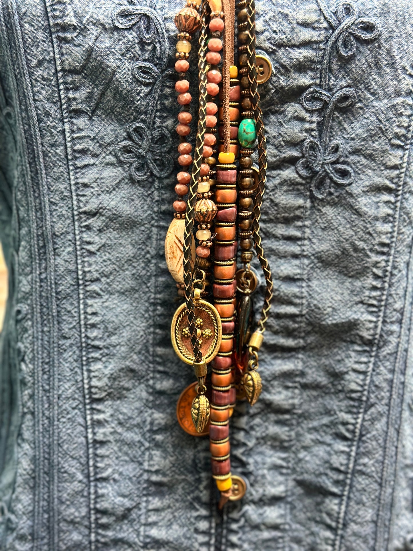 Necklace with beads and charms on denim jacket.