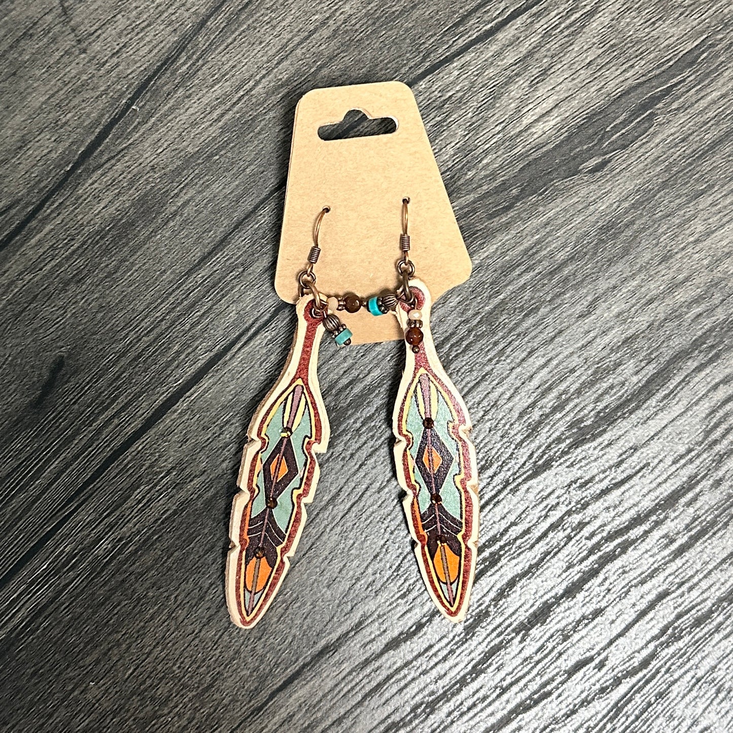 Feather-shaped earrings with colorful designs on a wooden surface.