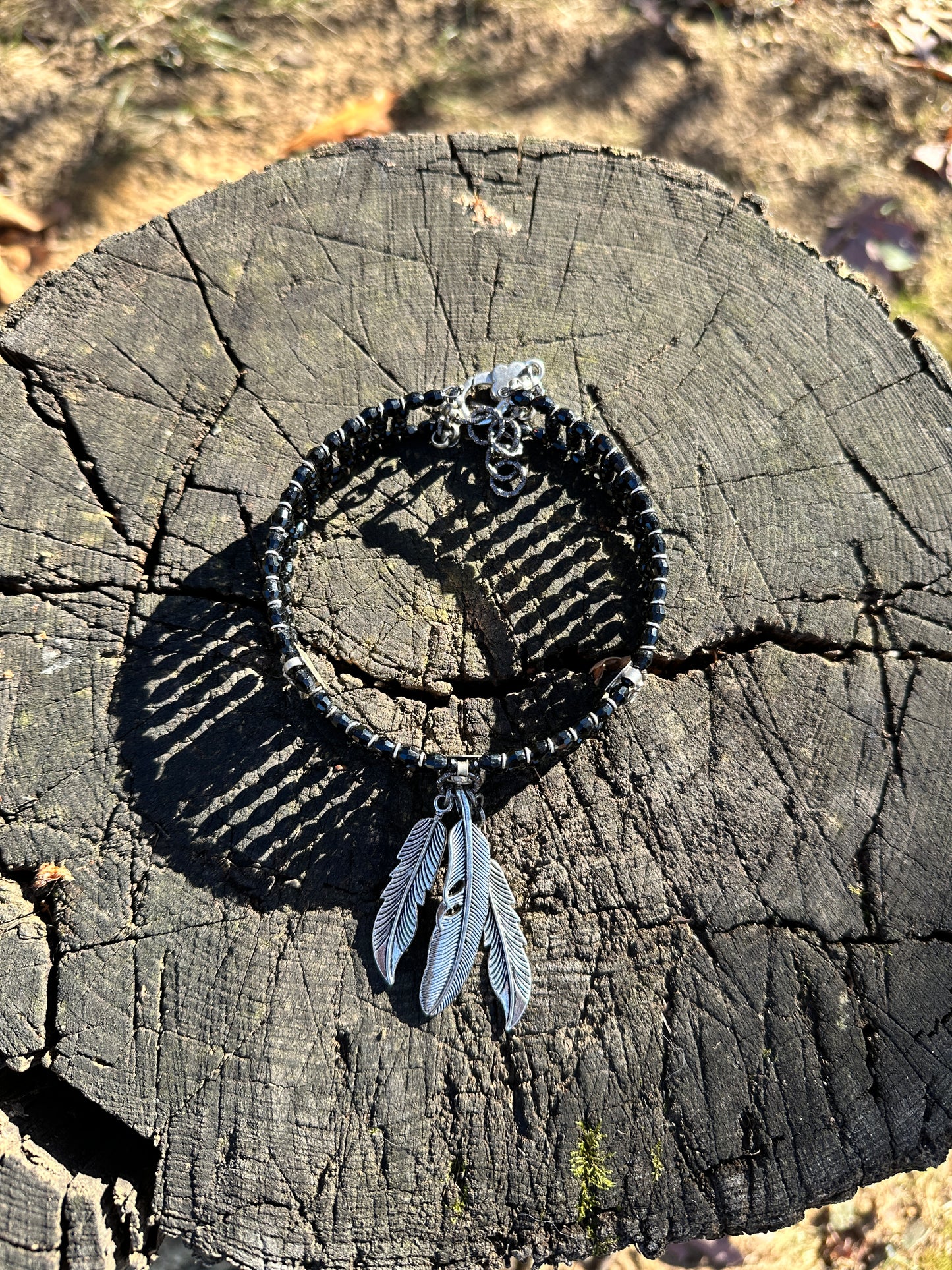 Black beaded bracelet with feather charm on wood.