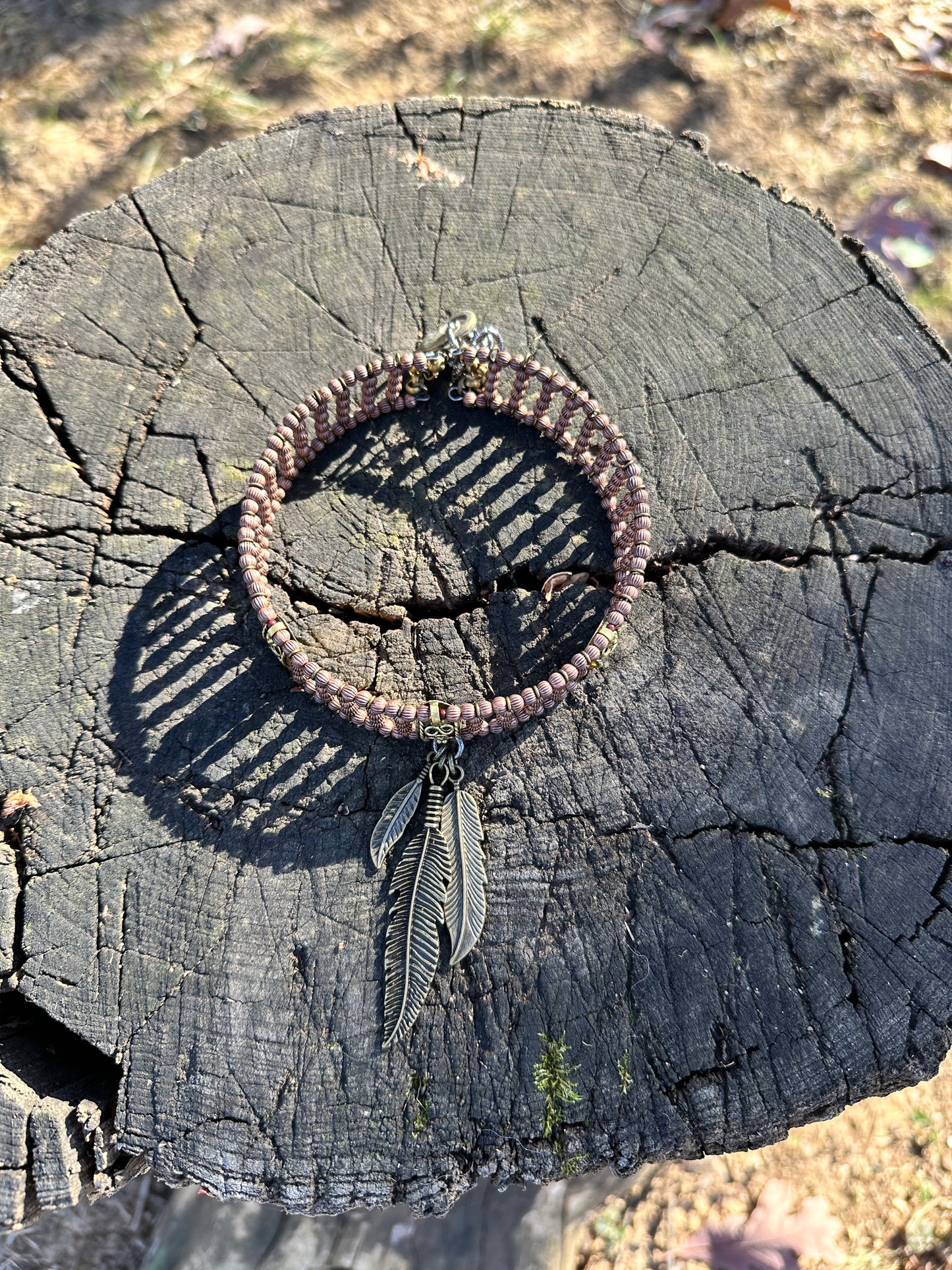Beaded bracelet with feather charm on wood stump.